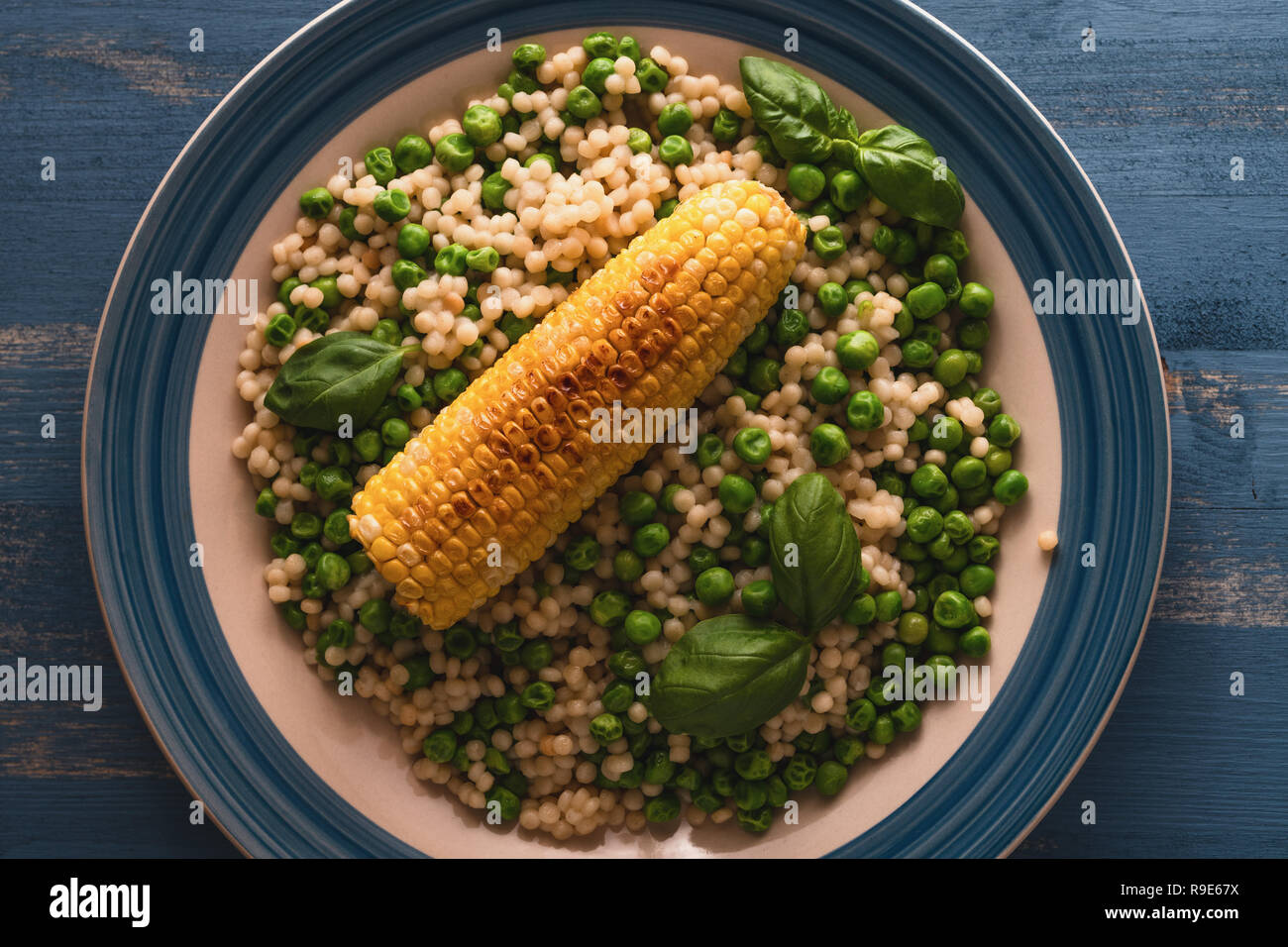 Couscous and sweet corn with green peas and fresh basil on a plate, top