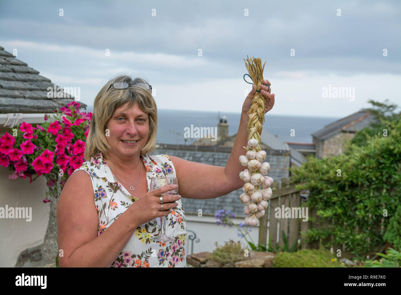 Woman holding up a string of plaited garlic that she has just made holding a glass of wine Stock Photo