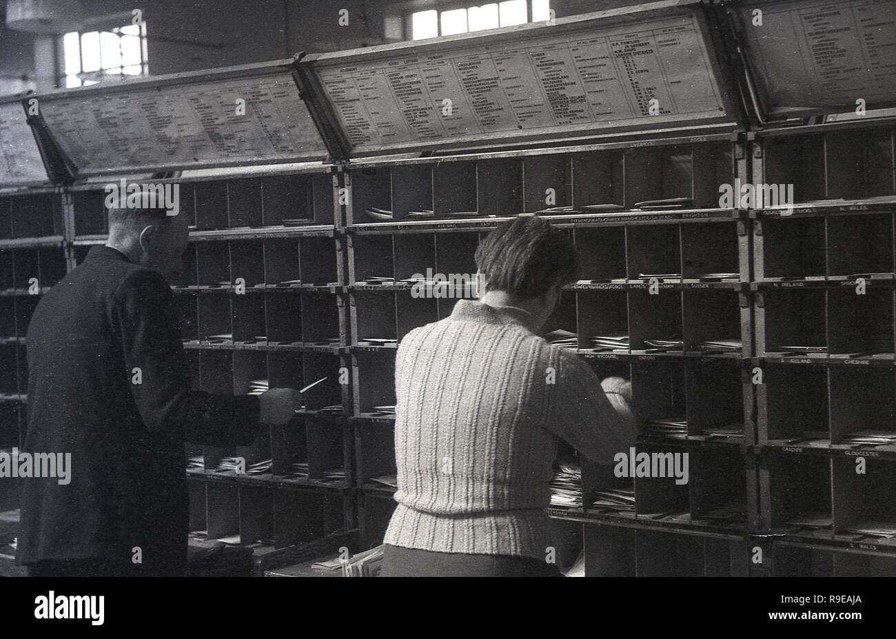1948, two Royal Mail staff workng inside a postal sorting office, England, UK. Picture shows them putting letters into small cubicles for the different streets. Stock Photo