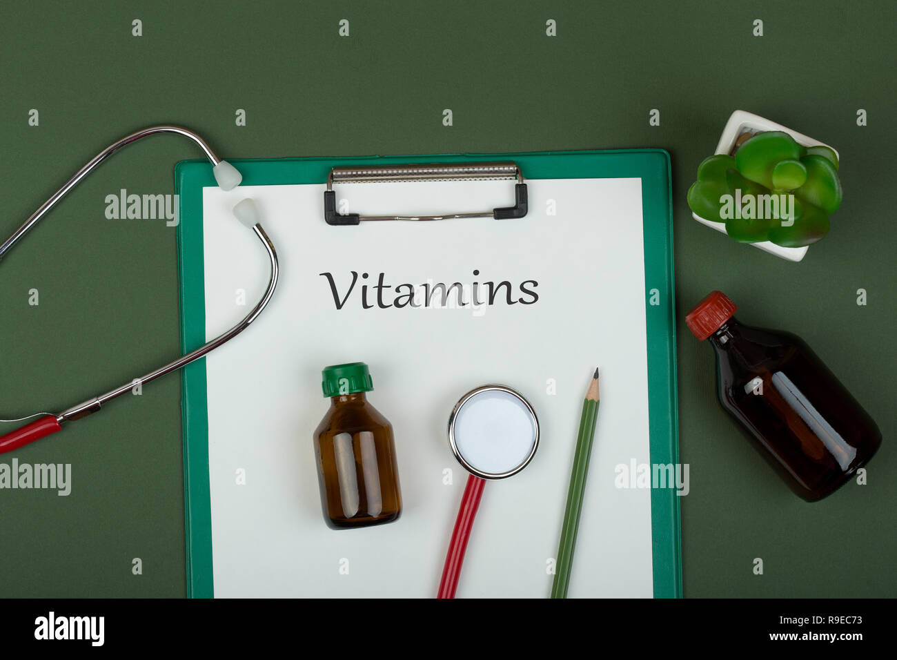 Doctor workplace - red stethoscope, medical bottles and clipboard with text 'Vitamins' on green paper background Stock Photo