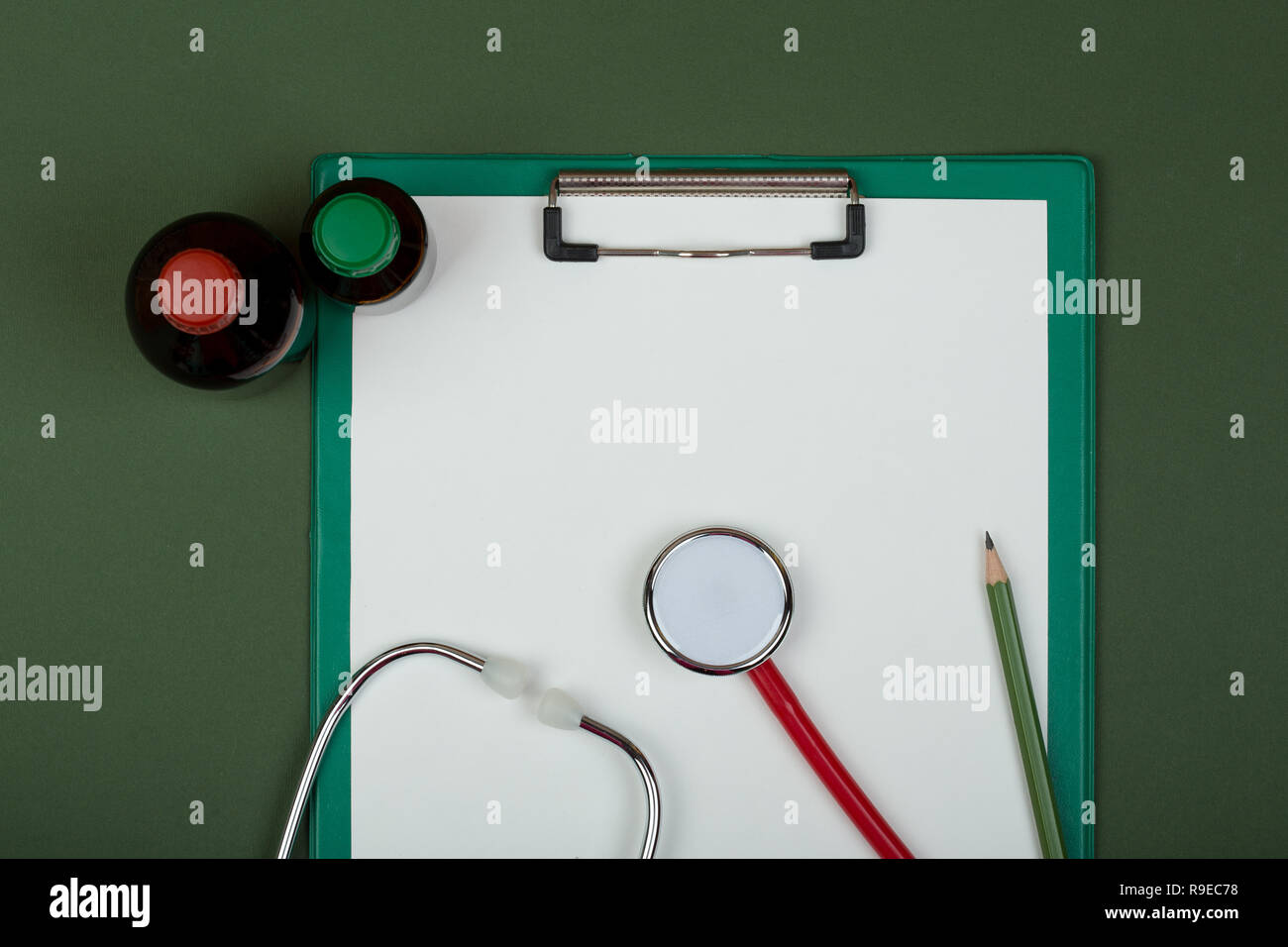 Doctor workplace - red stethoscope, medical bottles and empty clipboard on green paper background Stock Photo