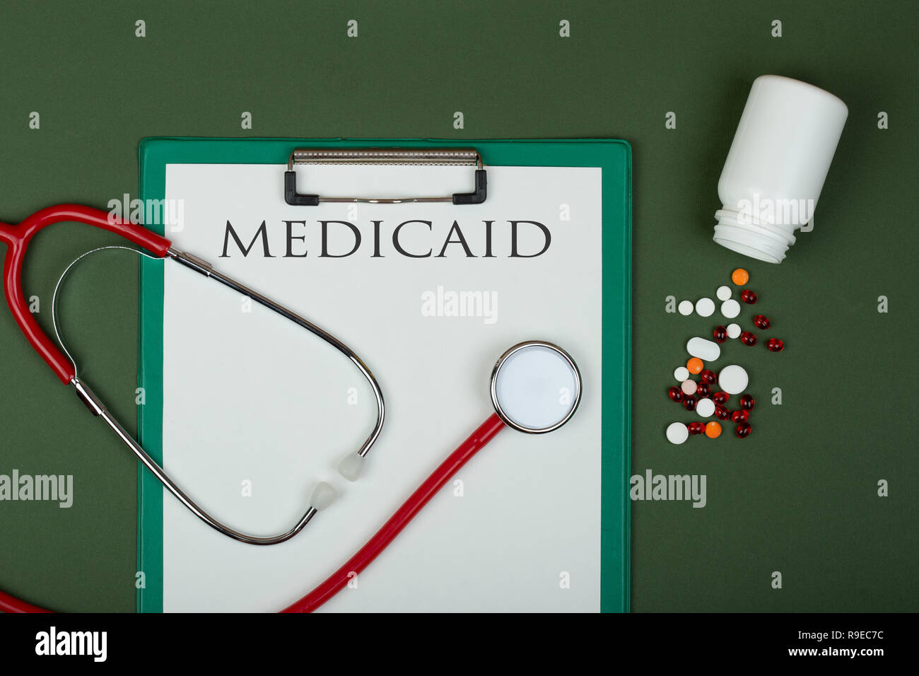 Doctor workplace - red stethoscope, pills, medical bottle and clipboard with text 'medicaid' on green paper background Stock Photo