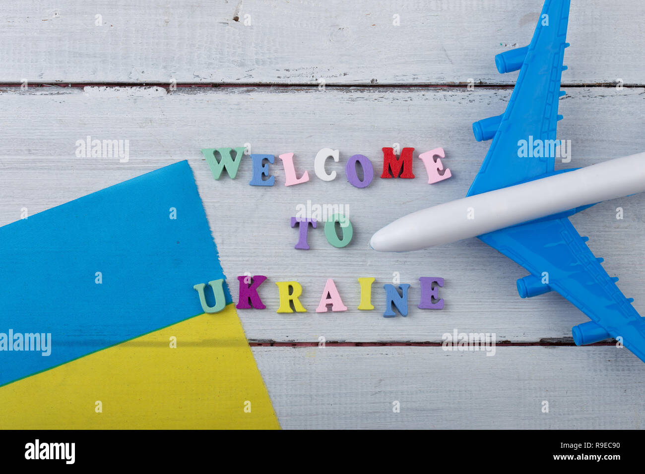 Travel time - colorful wooden letters with text 'Welcome to Ukraine' , flag of the Ukraine, airplane model, passport on white wooden background Stock Photo