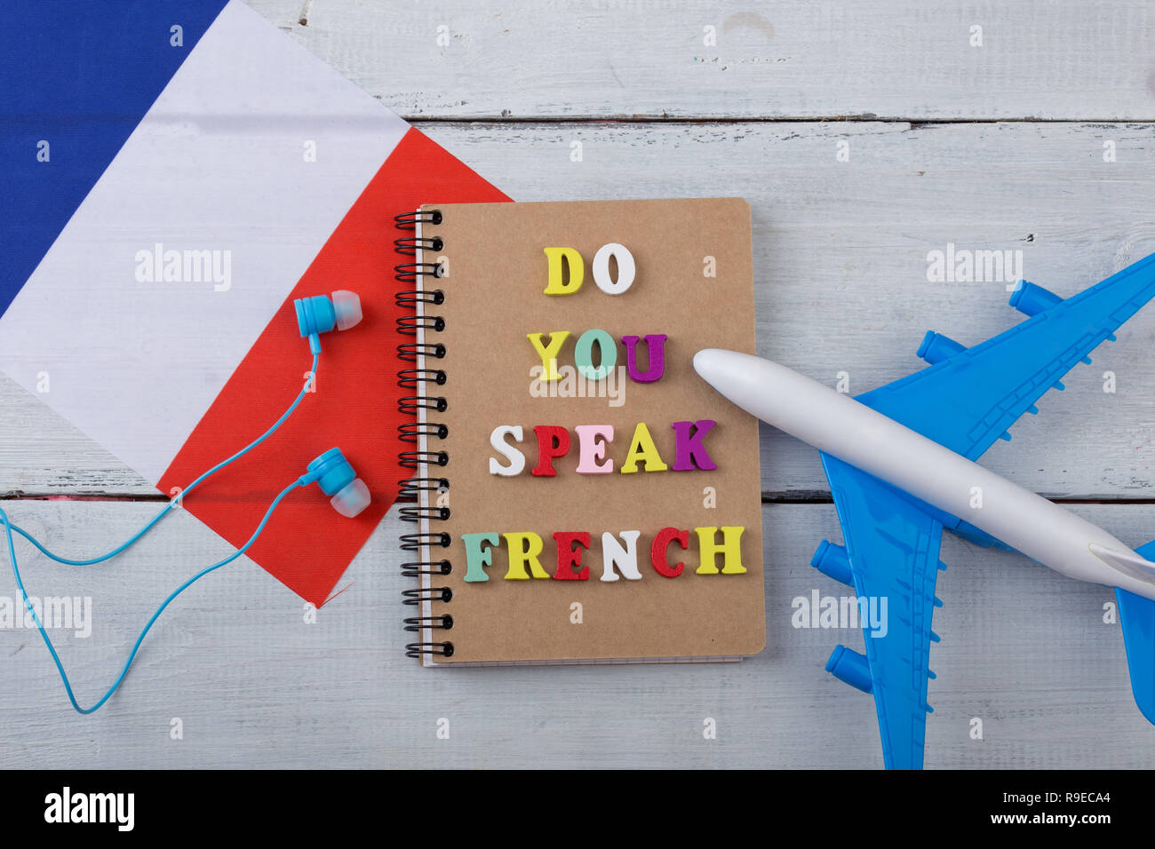 Concept of learning French language - colorful letters with text 'Do you speak French', flag of the France, airplane, headphones on white wooden backg Stock Photo