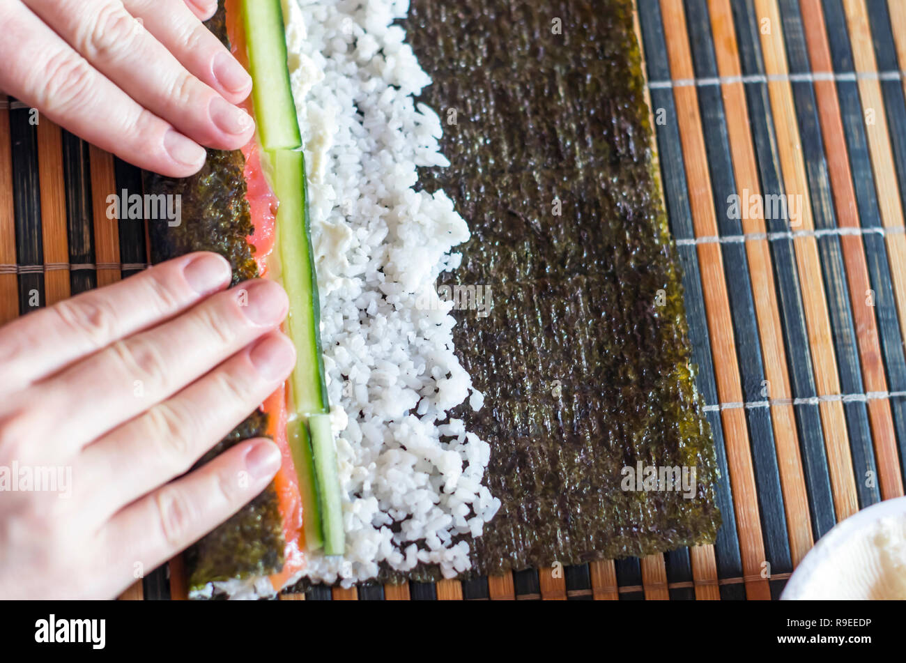 https://c8.alamy.com/comp/R9EEDP/making-sushi-rolls-at-home-female-hands-roll-nori-seaweed-sheet-on-a-bamboo-mat-ingredients-salmon-fish-strips-cucumber-sticks-cream-cheese-and-R9EEDP.jpg