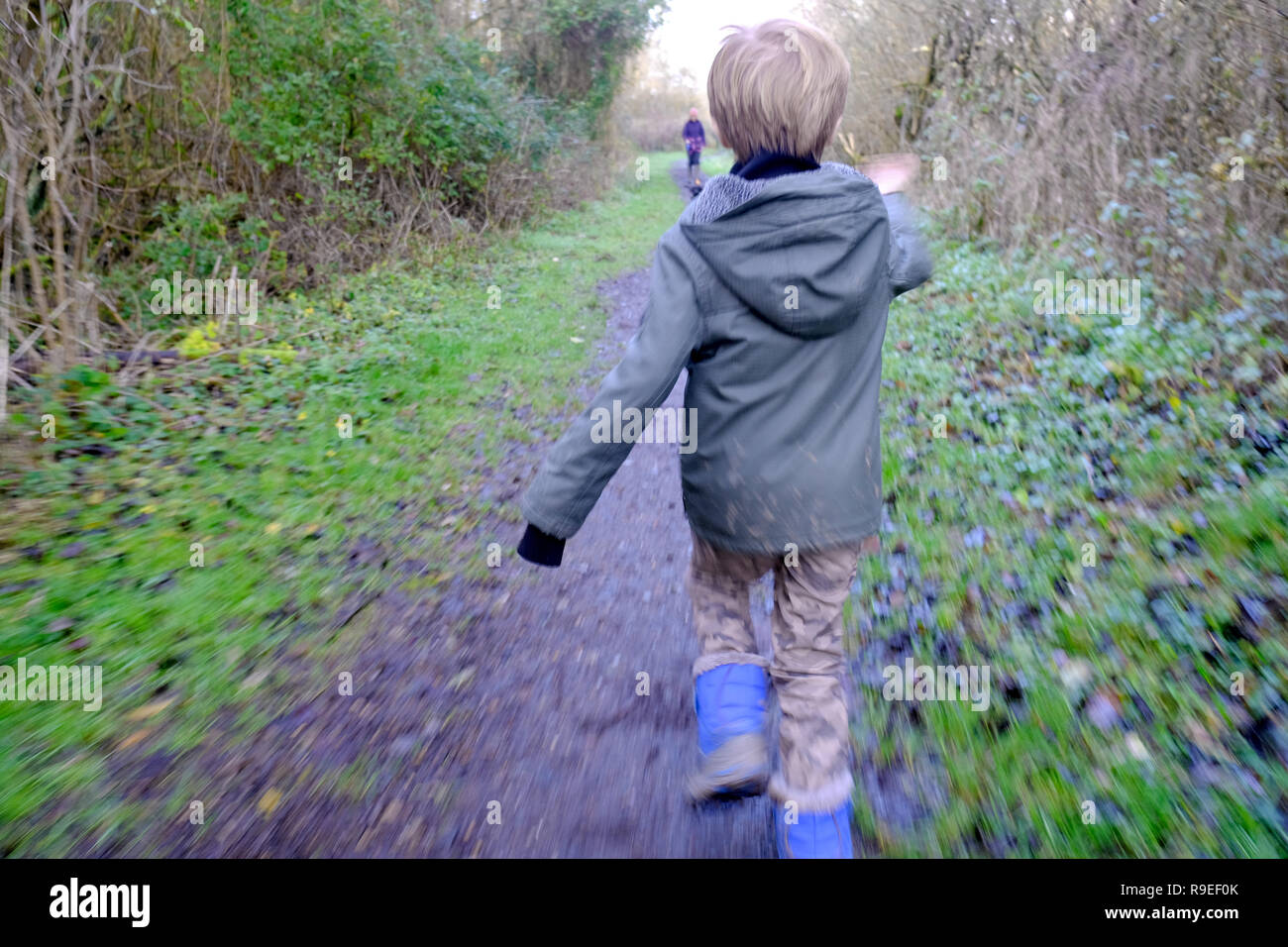 7 year old boy running to his mother and dog on a woodland footpath Stock Photo