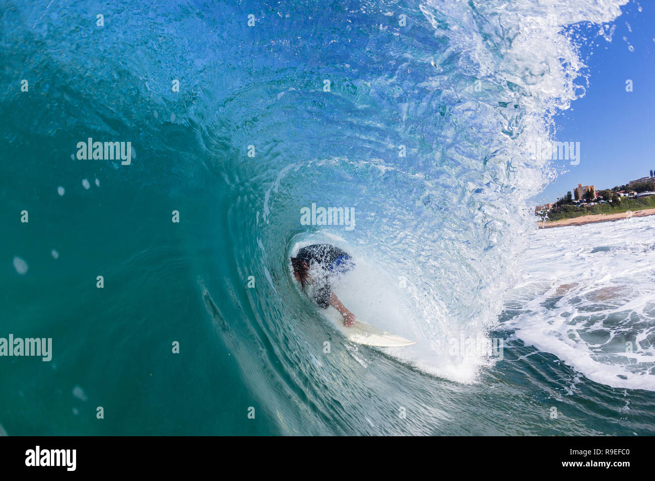 Surfer surfing riding  inside hollow ocean wave tube loosing balance crashing falling wipe-out in progress swimming water action photo. Stock Photo