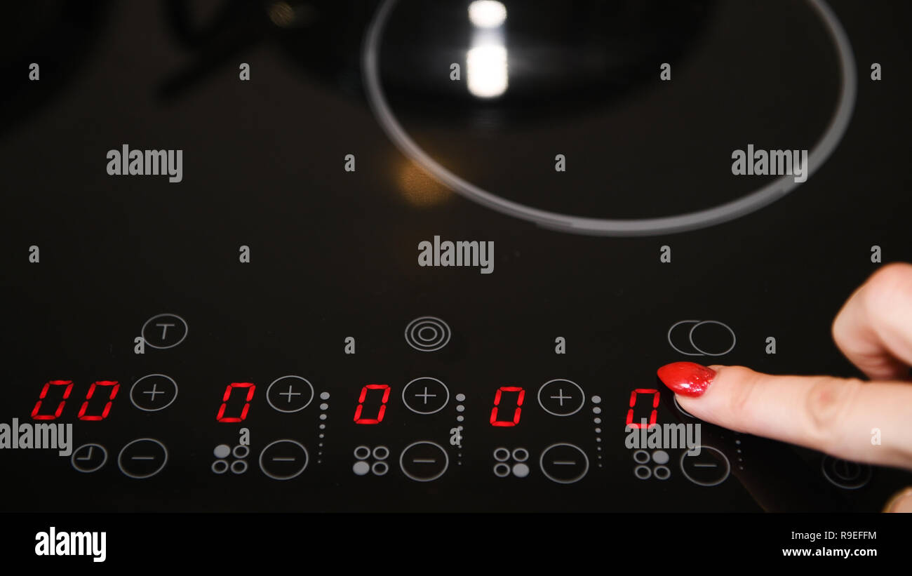 Female finger operating electric stove, nicely manicured finger nails