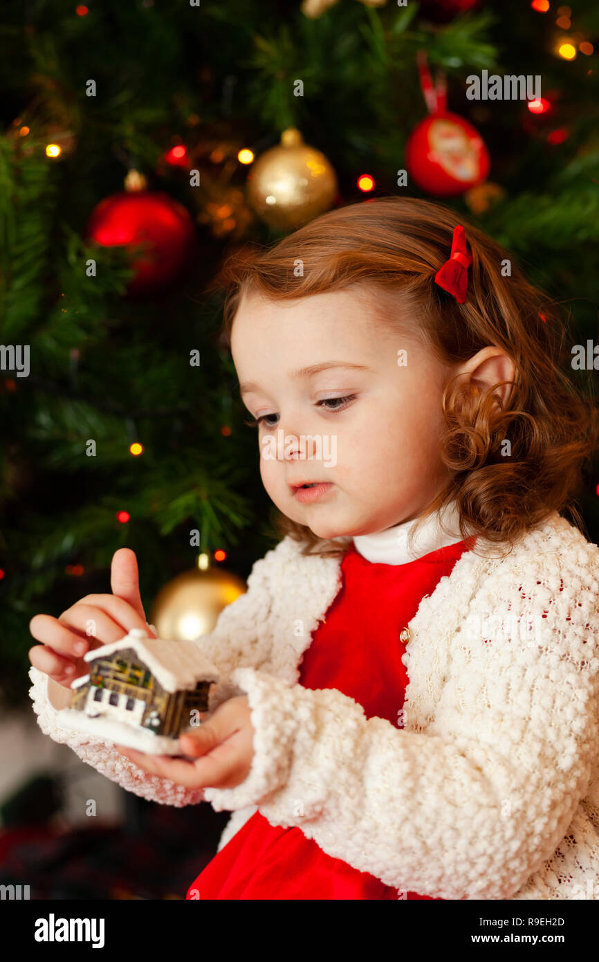Portrait of a beautiful little child with red dress near Christmas tree. Stock Photo