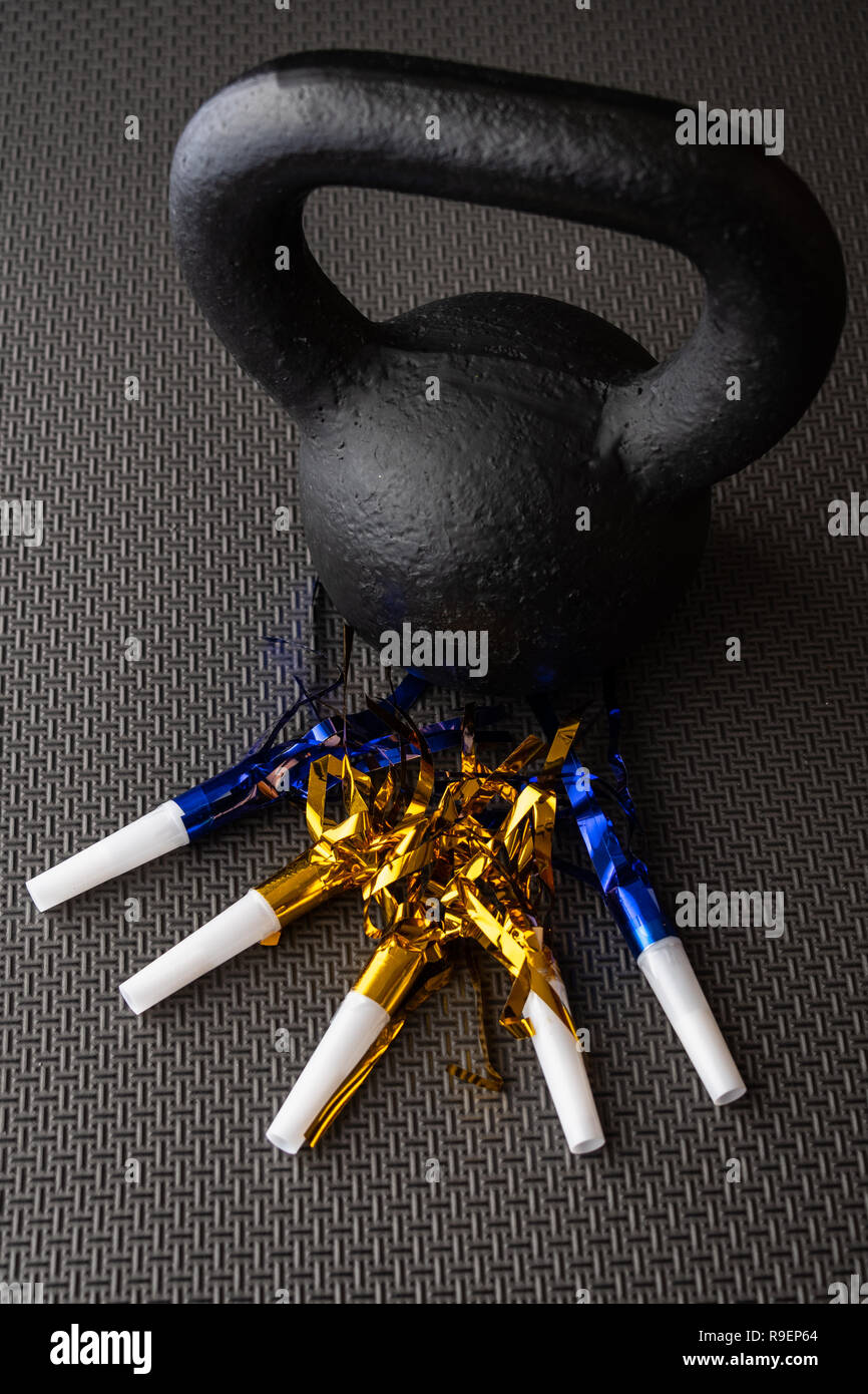 Black kettlebell on a black gym floor with blue and gold noisemakers to ...