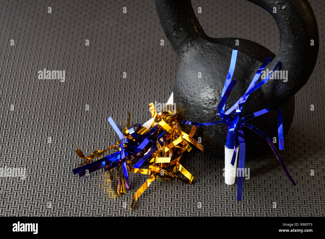 Black kettlebell on a black gym floor with blue and gold noisemakers to ...