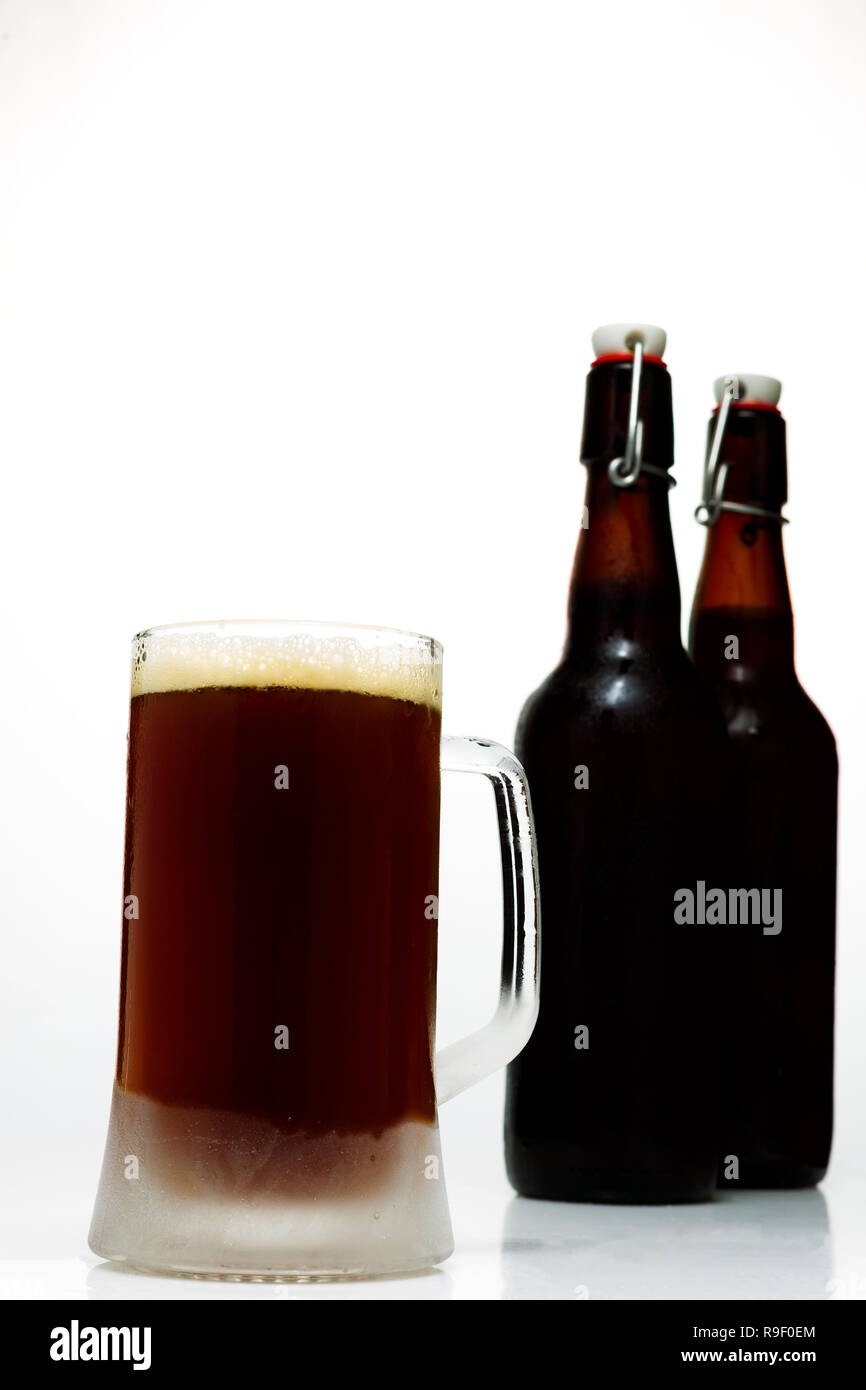 Beer glass with dark beer and two full beer bottles on a white