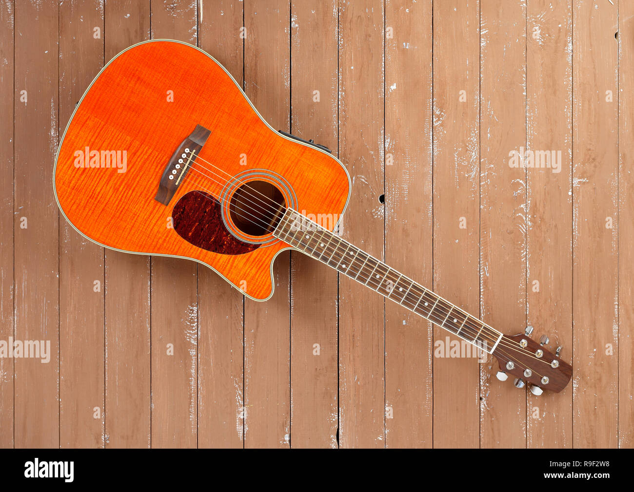 Musical instrument - Orange Flame maple acoustic cutaway tiger maple wood  guitar on a blue wood background Stock Photo - Alamy