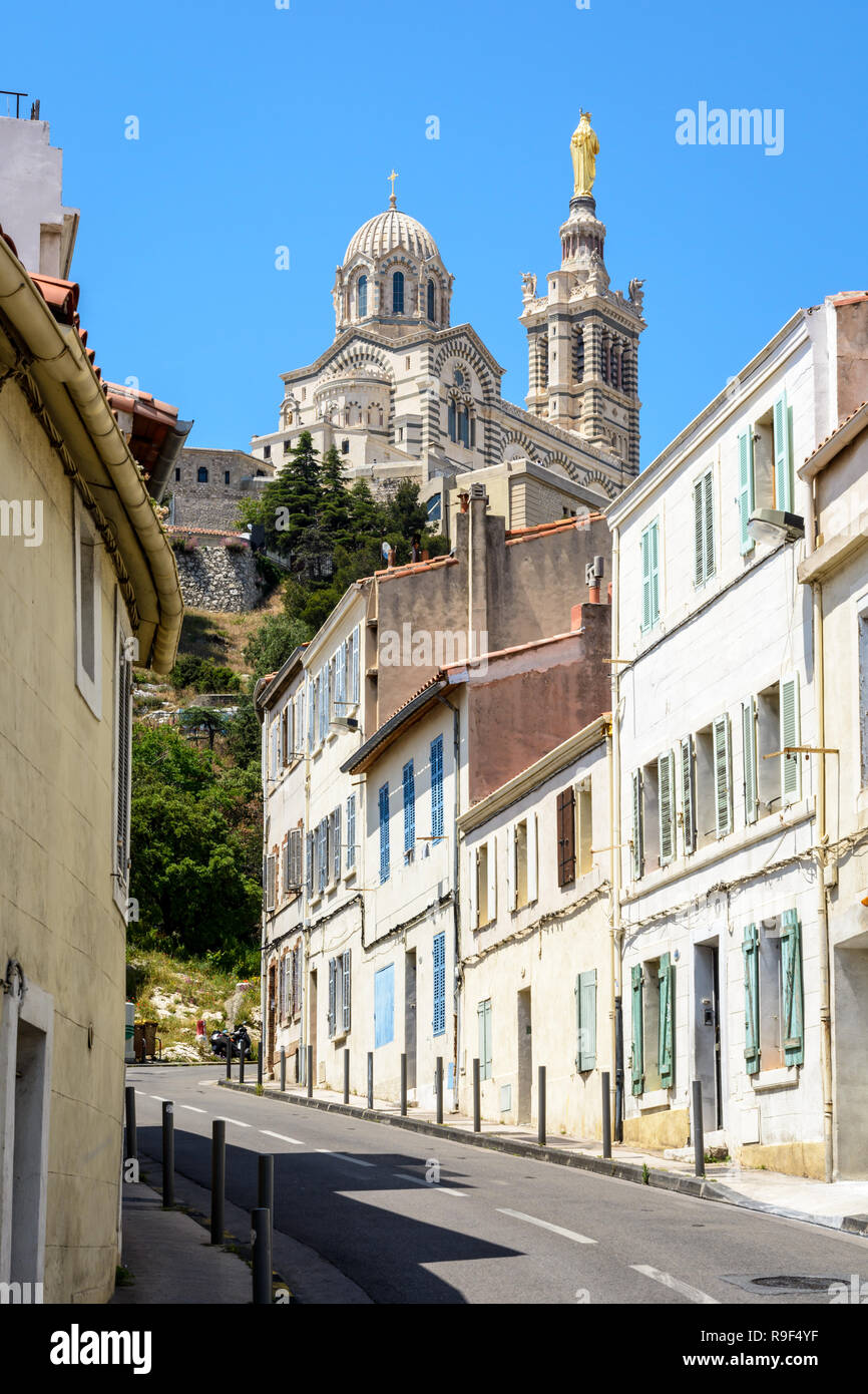A narrow sloping street bordered with old townhouses in Marseille, France, going up to Notre-Dame de la Garde basilica on top of the hill. Stock Photo