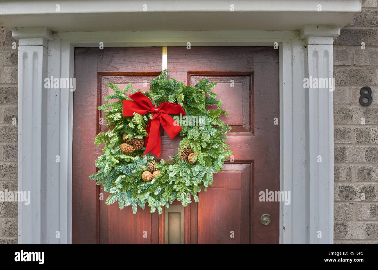 Advent wreath, consisting of a red ribbon, green foliage, and cones, on the front door of a house. Stock Photo