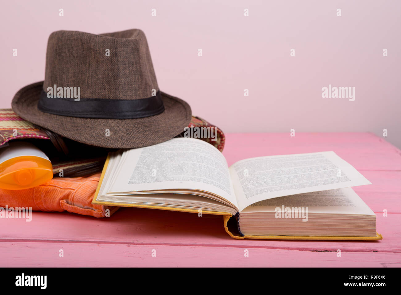 Summer accessories - straw beach bag, sun hat, open book, suntan lotion on pink wooden table Stock Photo
