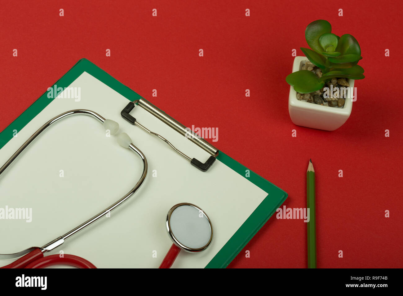 Doctor workplace - red stethoscope, pencil and empty green clipboard on red paper background Stock Photo