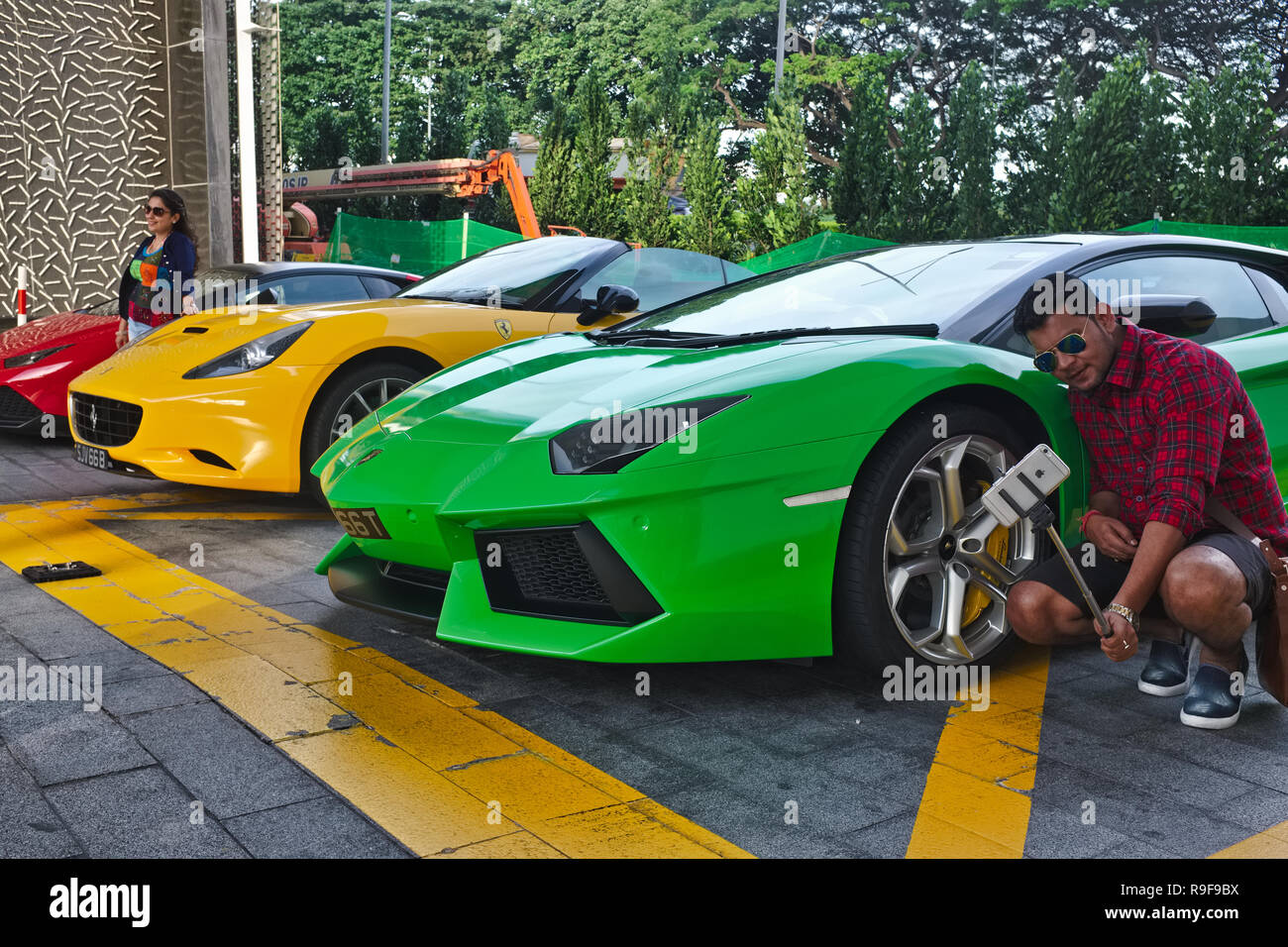 An Indian tourist takes a selfie in front of a Lamborghini Aventador and other luxury cars parked at Marina Bay Sands Hotel, Marina Bay, Singapore Stock Photo