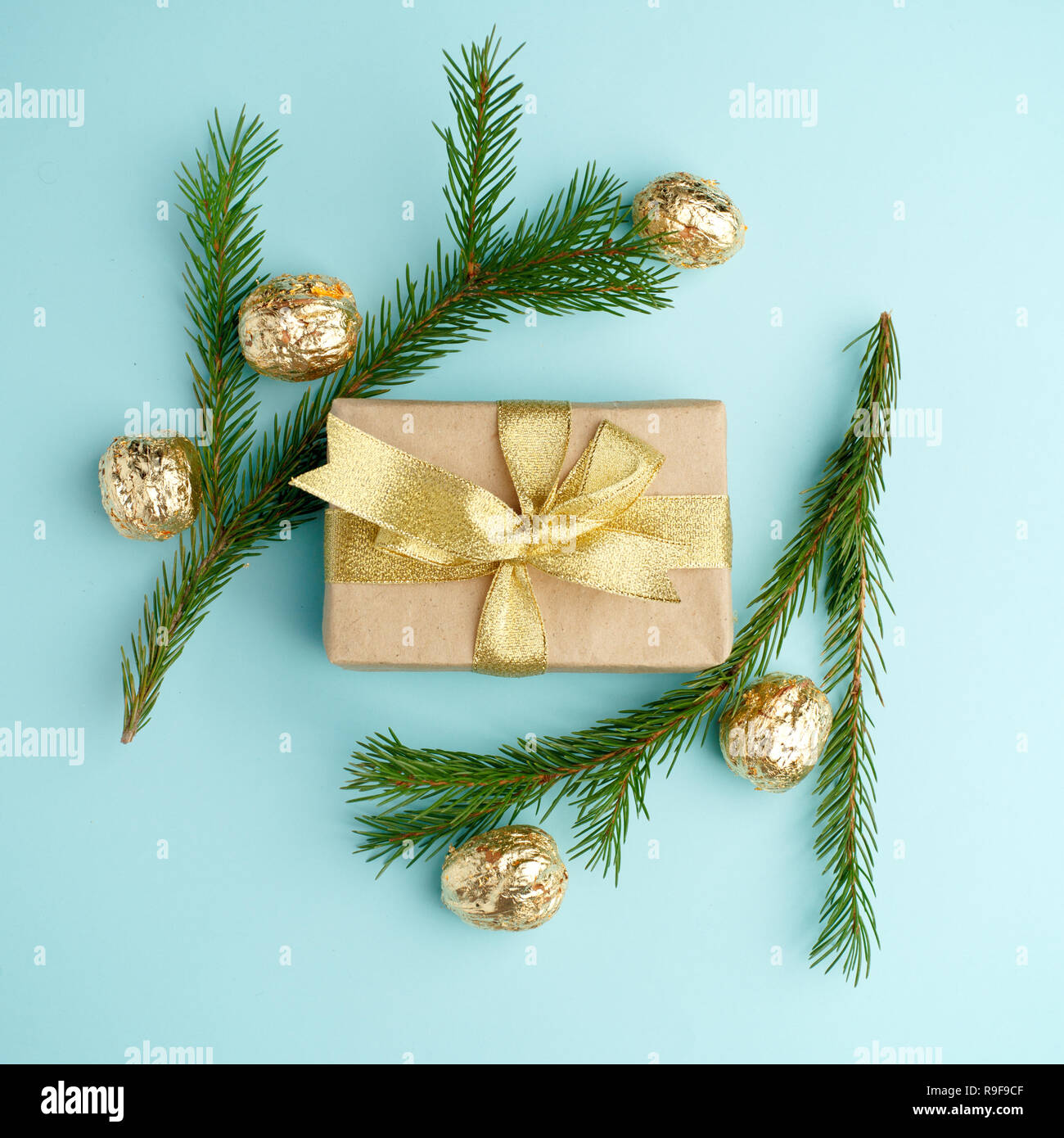 Creative Chistmas layout made of winter greenery, kraft gift box with golden ribbon and golden decoration on blue background. Flat lay, top view. Holi Stock Photo