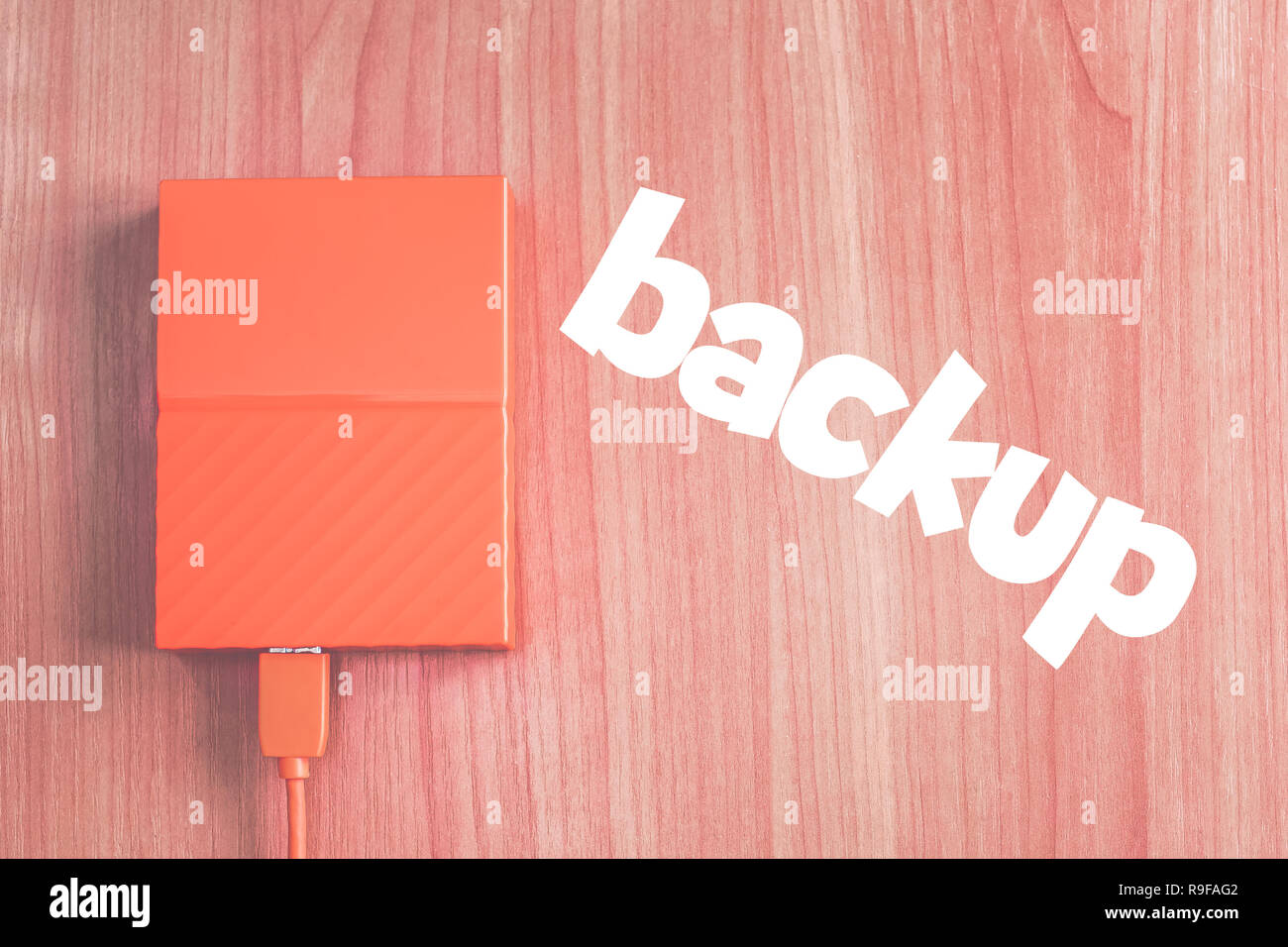 Portable external hard drive on the desk next to inscription 'BACKUP'. Stock Photo