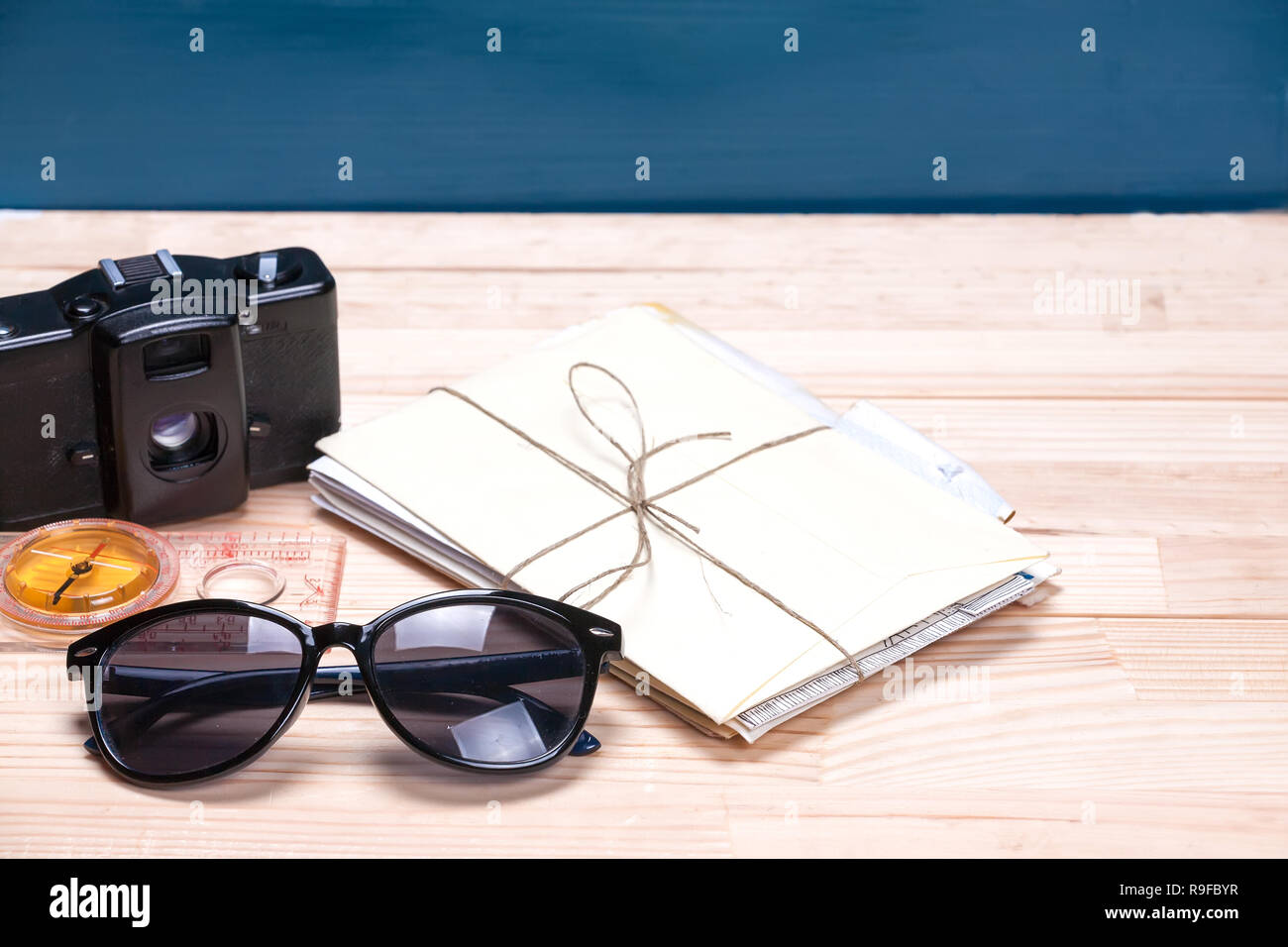 Sunglasses, compass, old film camera and a bunch of letters on a light and blue wooden background. Copy space to the right. Concept of summer travel d Stock Photo