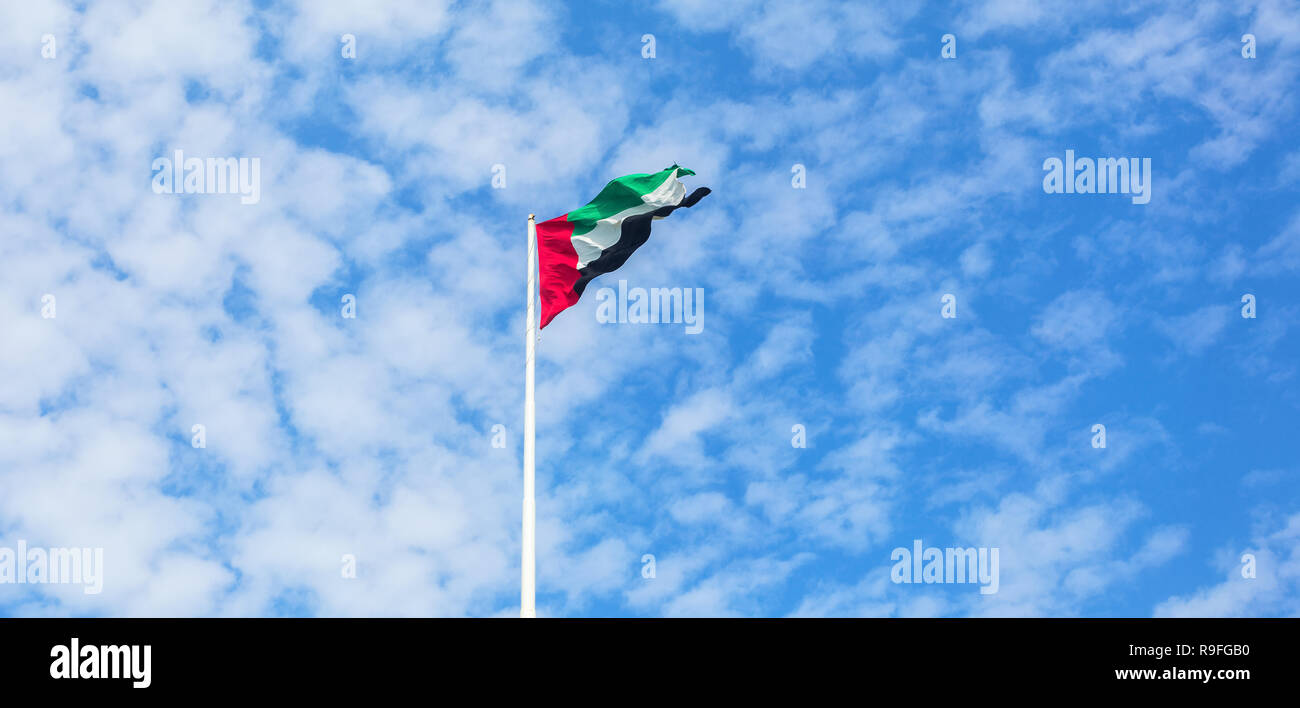 United Arab Emirates flag flying against beautiful blue sky with clouds. UAE celebrates it's national day on 2nd December every year. Stock Photo