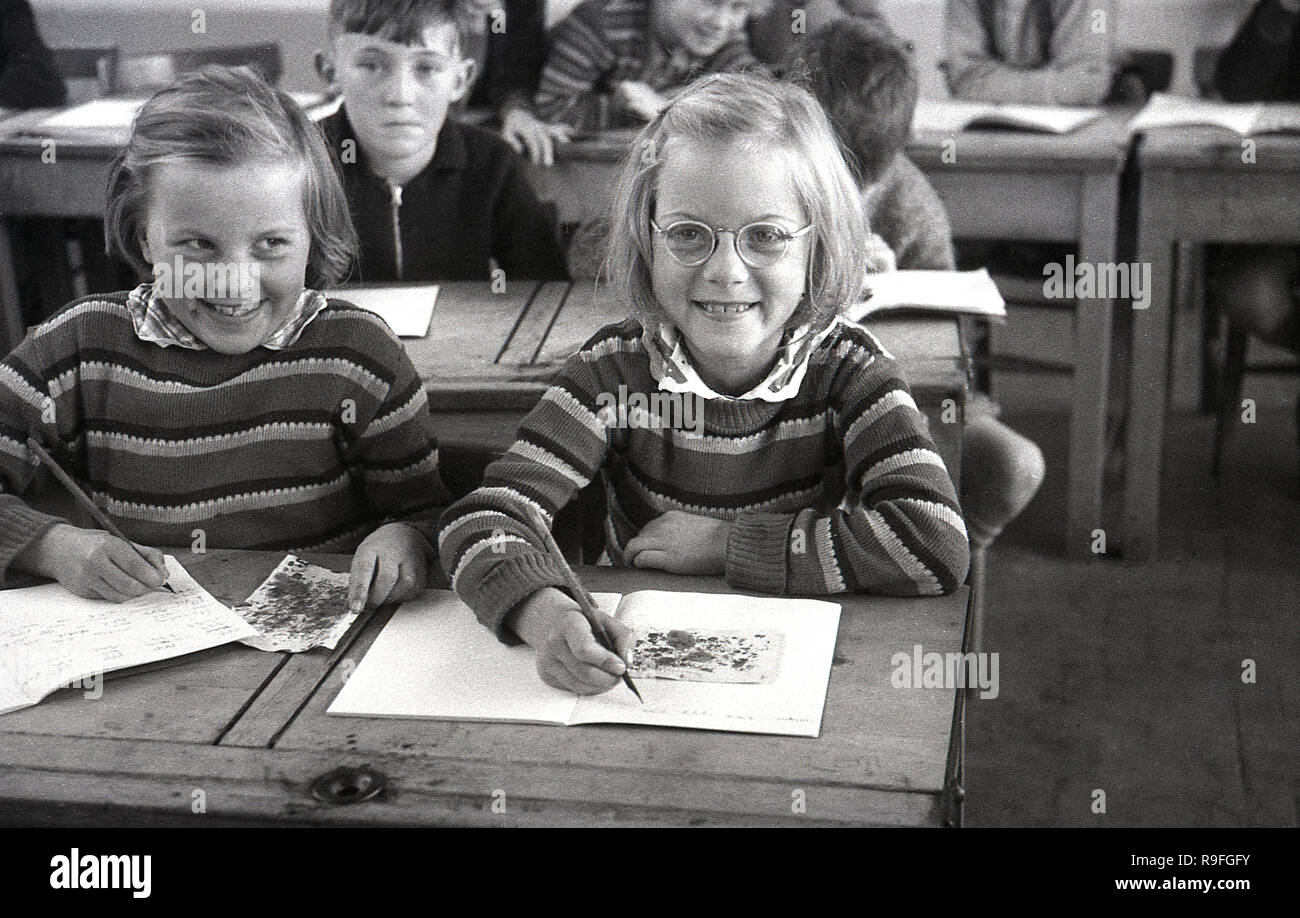 1950s, historical, primary school children, Langbourne School, England, UK. Picture shows two smiling young girls- possibly twin sisters as they look alike and are wearing identical jumpers - sitting next to each other at a wooden two-seater  desk doing an art class. Stock Photo