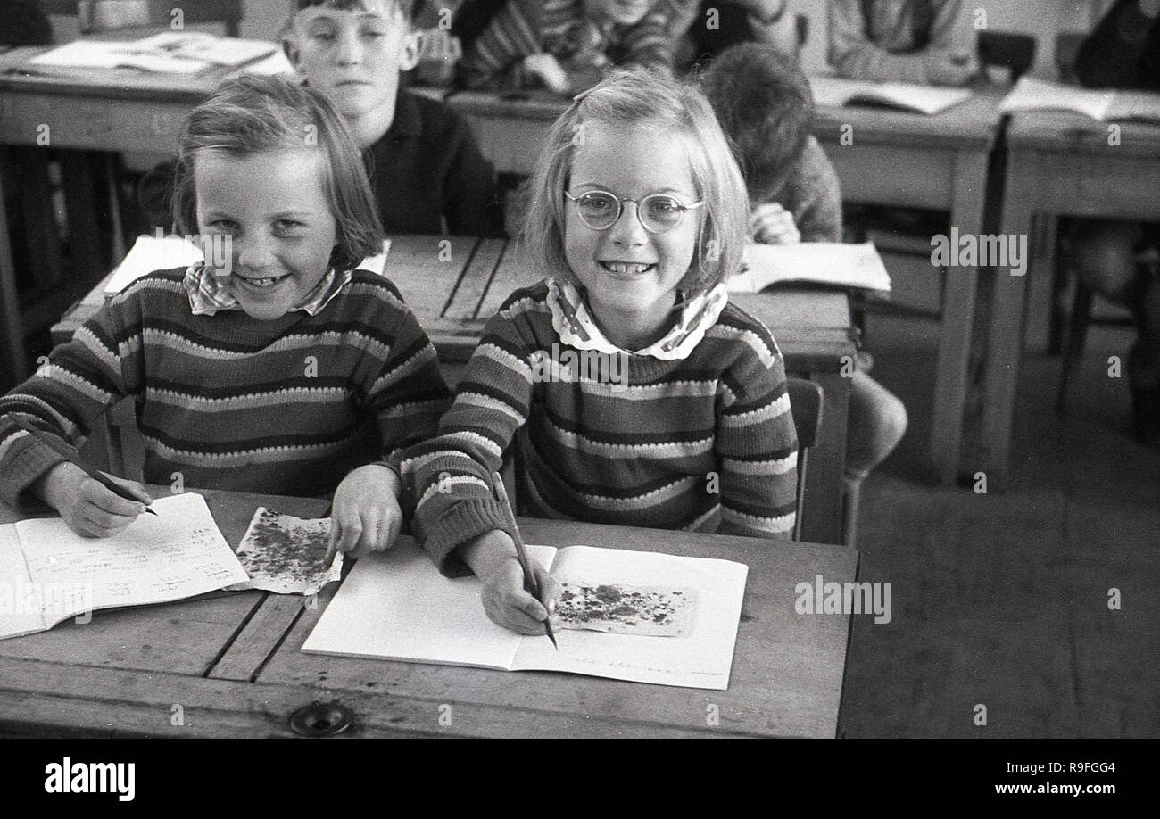 1950s, historical, primary school children, Langbourne School, England, UK. Picture shows two smiling young girls- possibly twin sisters as they look alike and are wearing identical jumpers - sitting next to each other at a wooden two-seater  desk doing an art class. Stock Photo