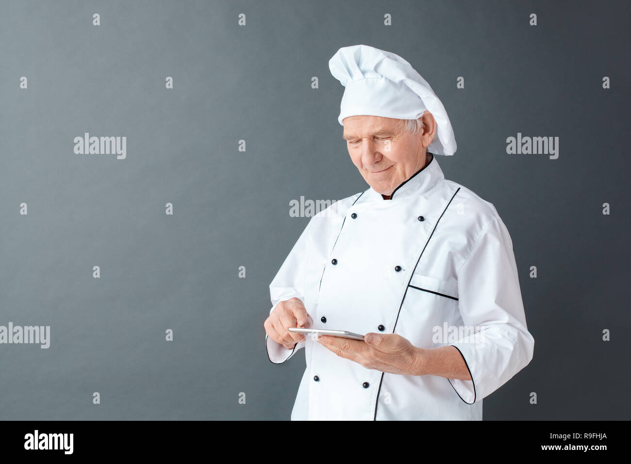 Senior male chef studio standing isolated on gray wall holding digital ...