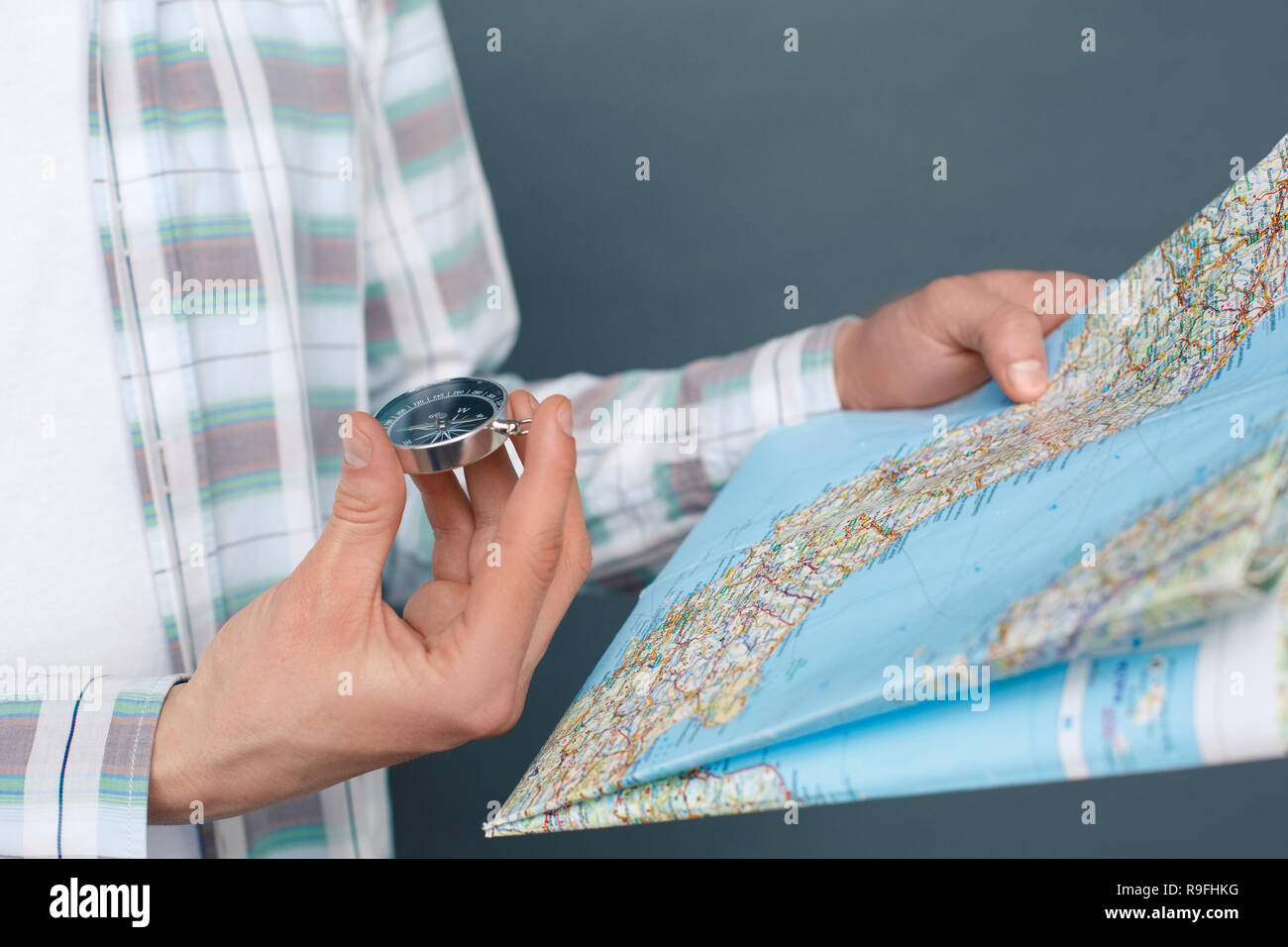 Young guy isolated on gray wall tourism concept standing holding map looking at compass needle close-up Stock Photo