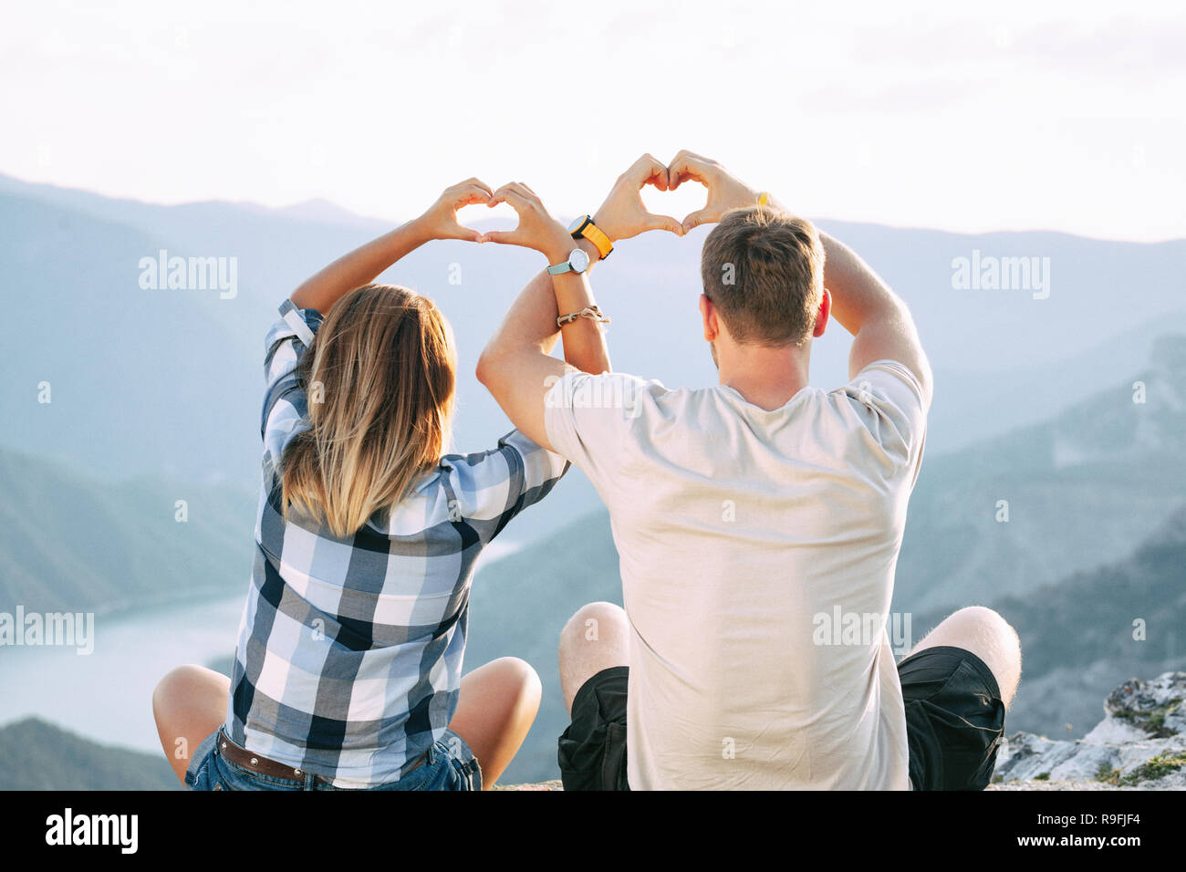 couple in love making hearts with their crossed hands while sitting on ...