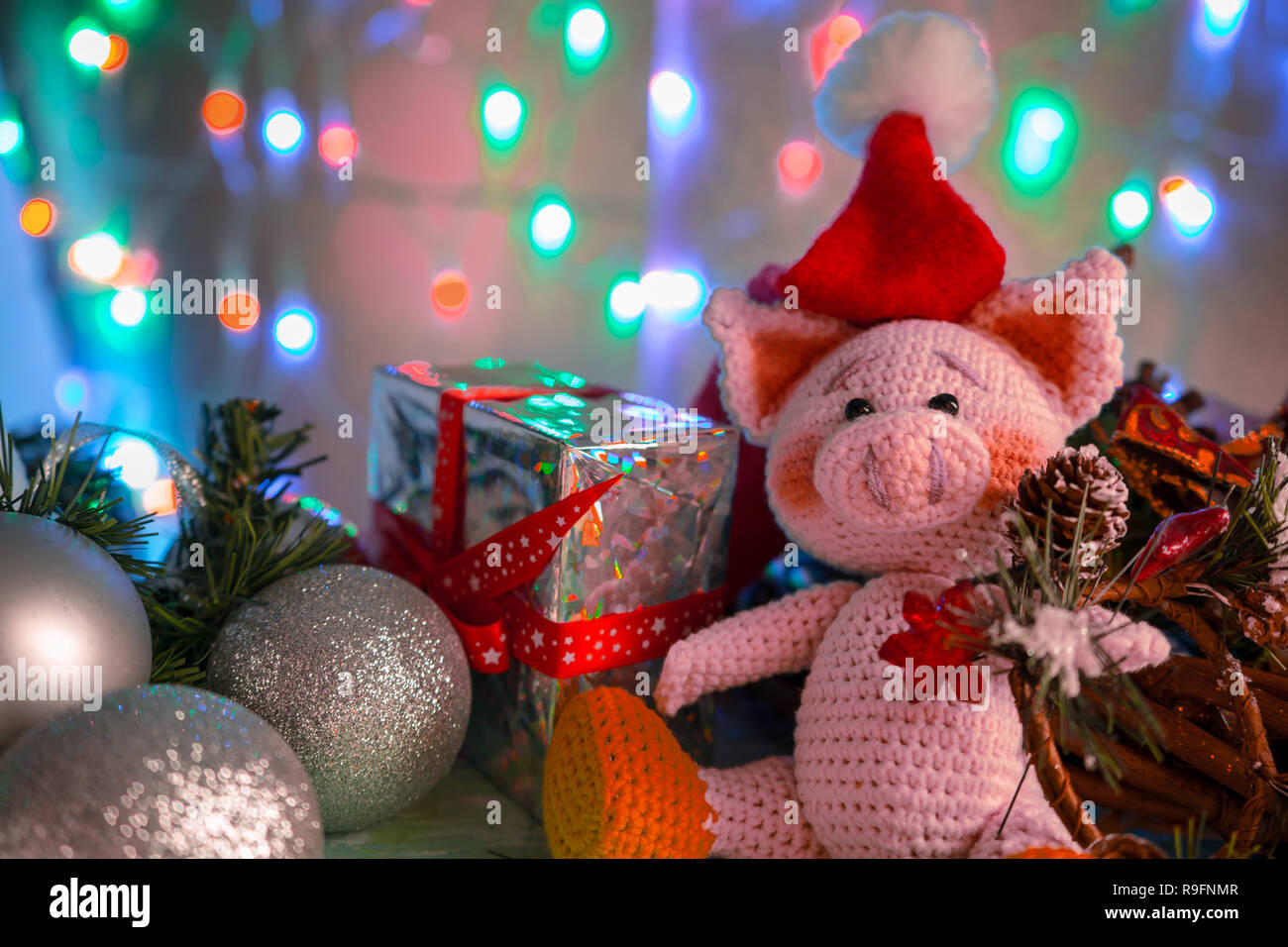Funny greeting card with new year 2019. Pink pig with xmas balls, gift and cone on background with illumination. Stock Photo