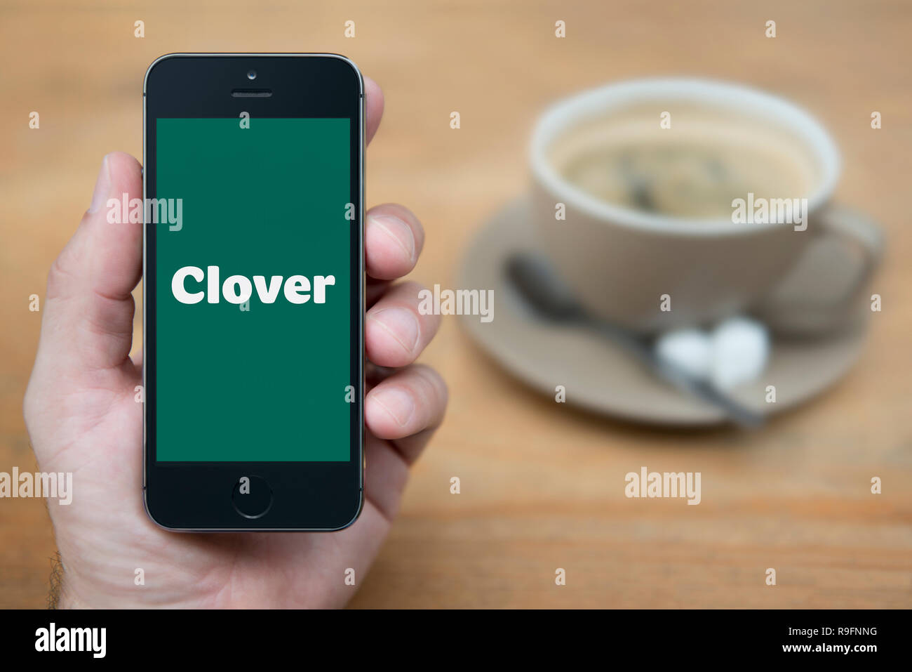 A man looks at his iPhone which displays the Clover logo (Editorial use only). Stock Photo