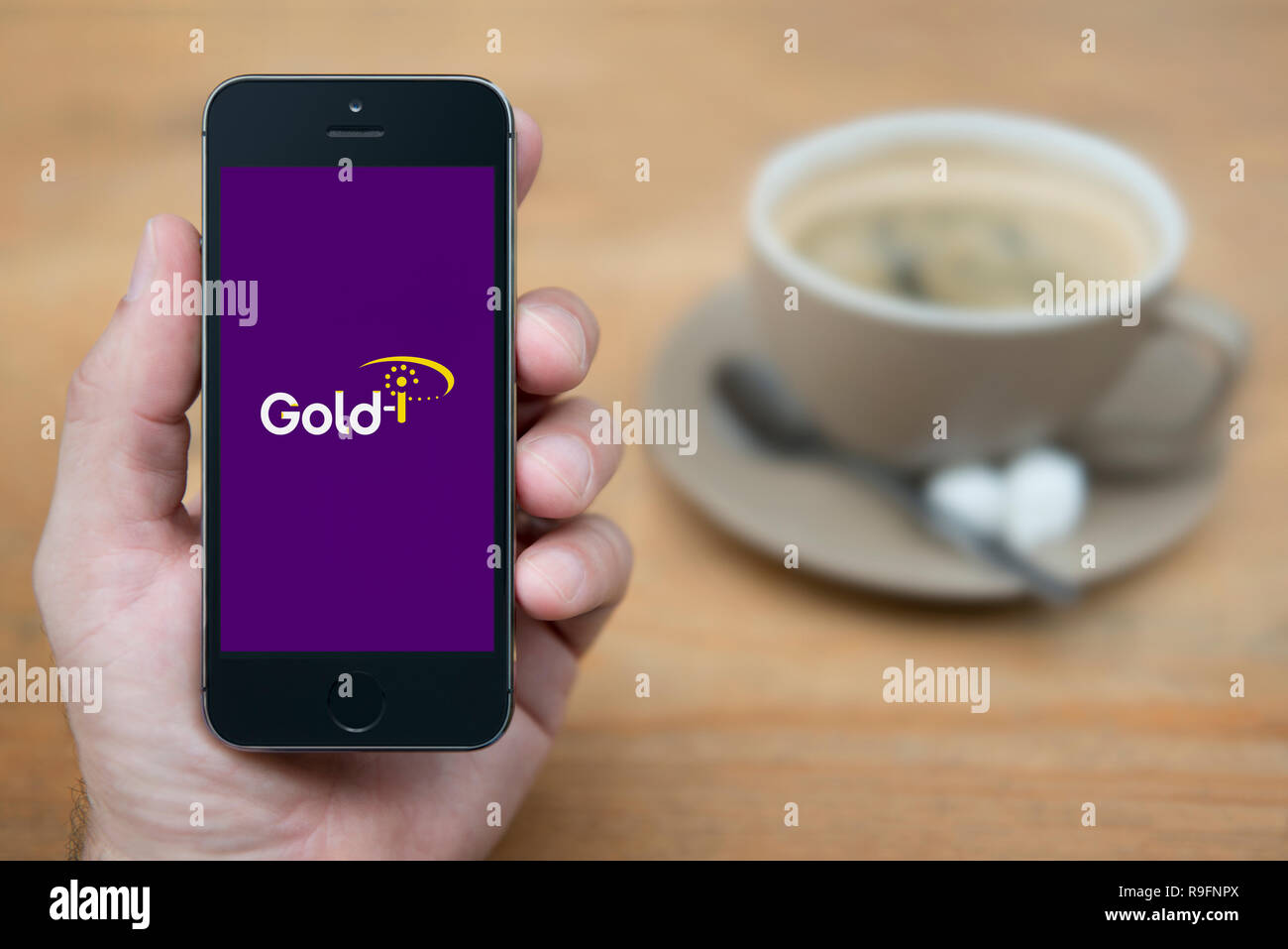 A man looks at his iPhone which displays the Gold-i logo (Editorial use only). Stock Photo