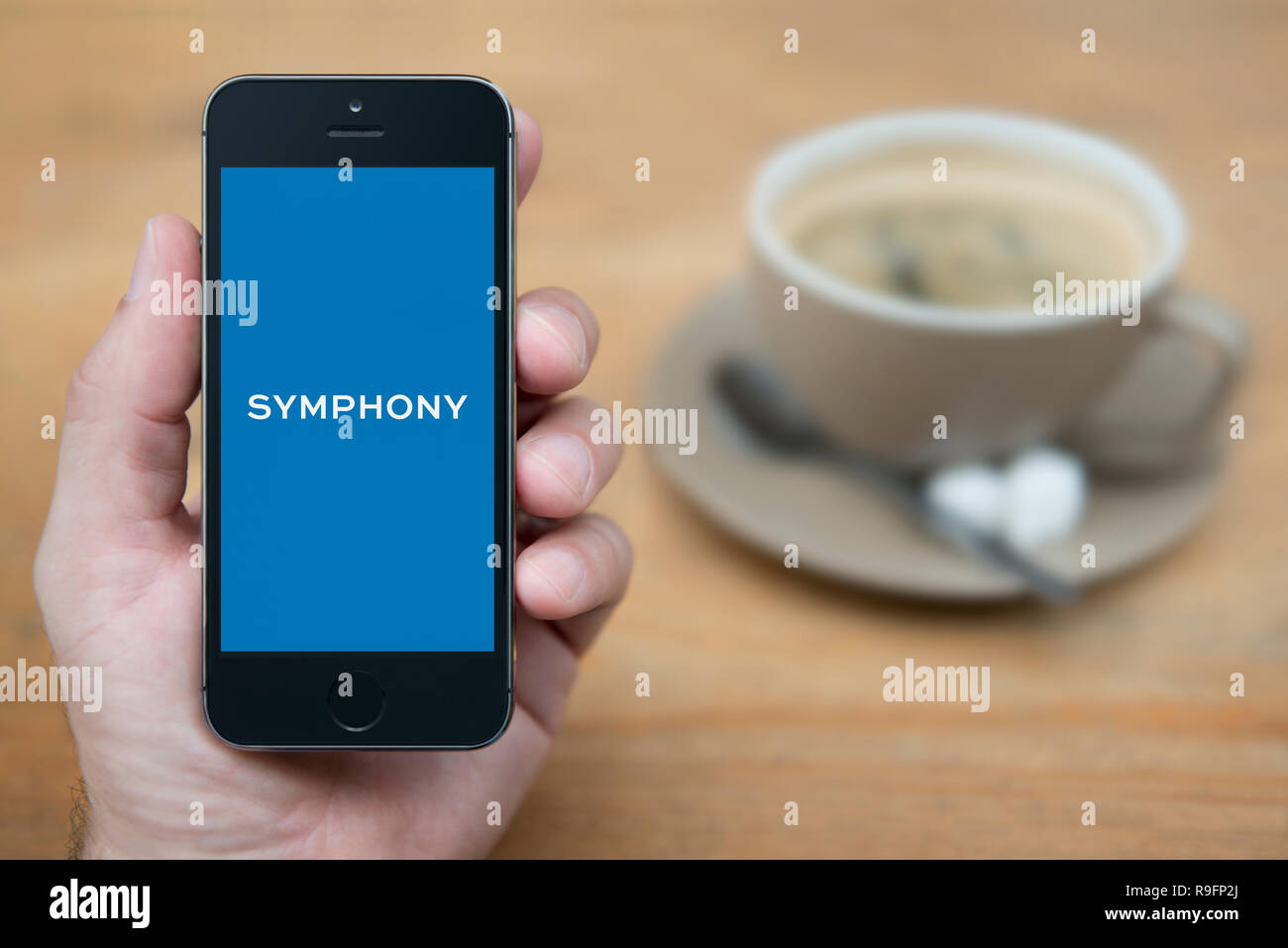 A man looks at his iPhone which displays the Symphony logo (Editorial use only). Stock Photo