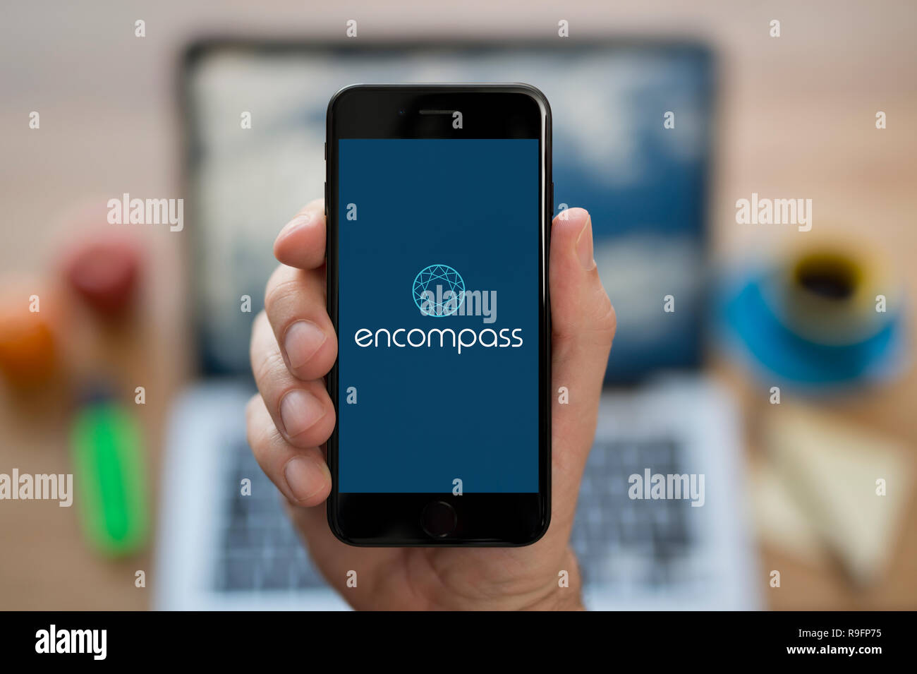 A man looks at his iPhone which displays the Encompass Corporation logo (Editorial use only). Stock Photo