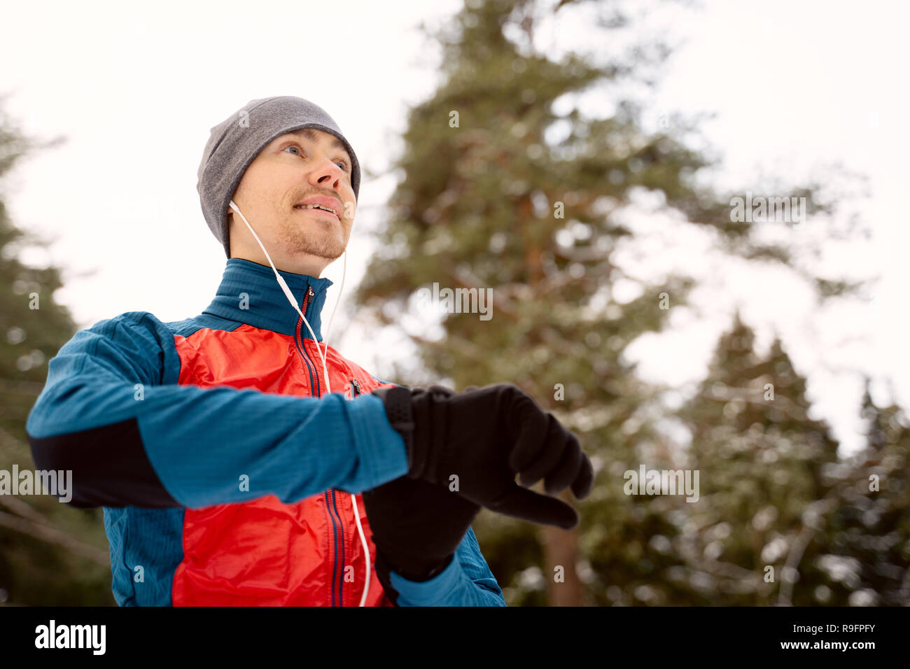 Runner wearing warm sporty clothes in headphones looks at a modern smart clock Stock Photo