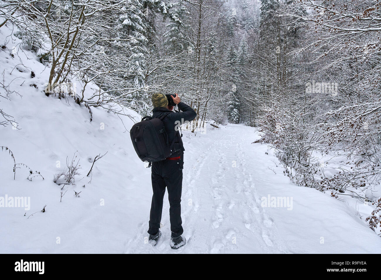 Tourist with camera and backpack hiking on a snowy trail in the ...