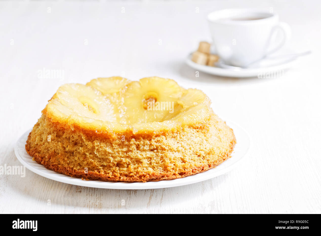 Pineapple Upside Down Cake and cup of tea on white wooden table. Shallow focus. High key. Stock Photo