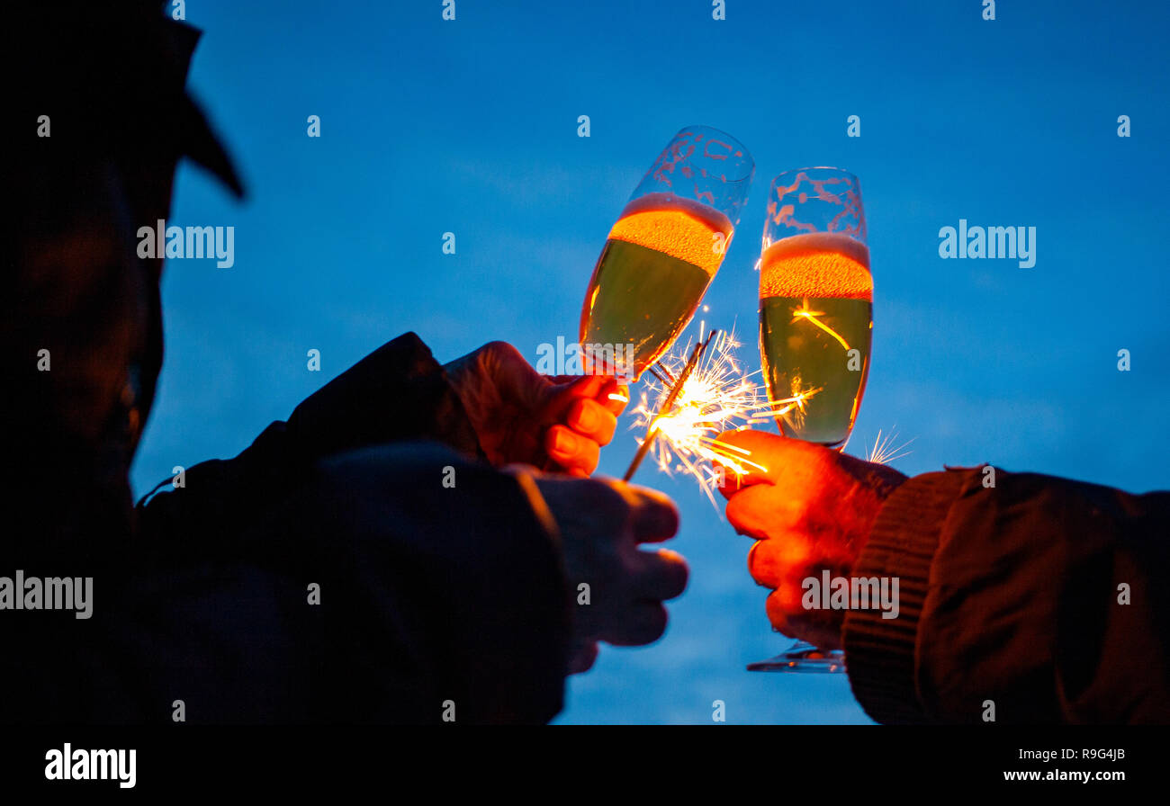hands of elderly couple holding sparkles and glasses of champagne celebrating New Year Stock Photo