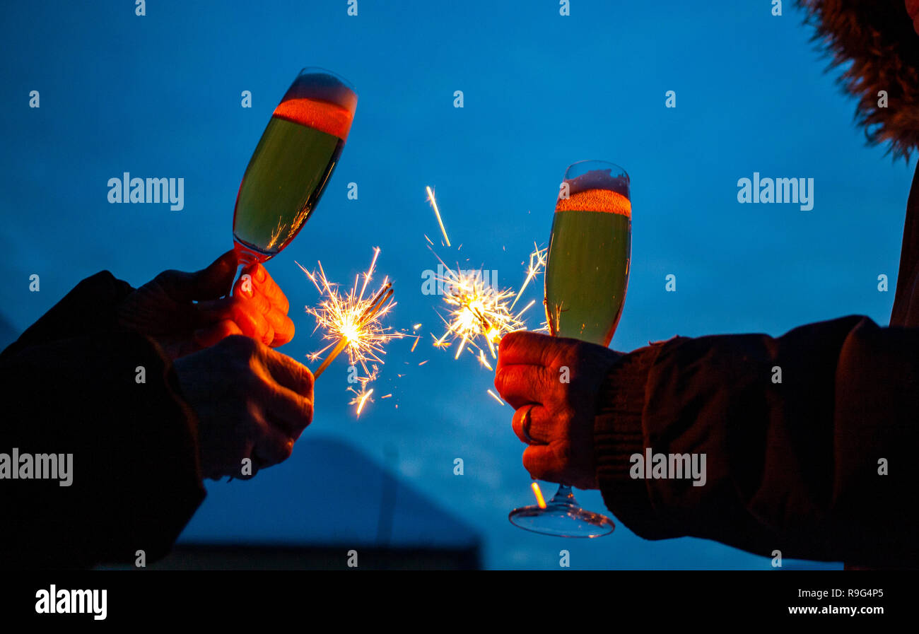 hands of elderly couple holding sparkles and glasses of champagne celebrating New Year Stock Photo