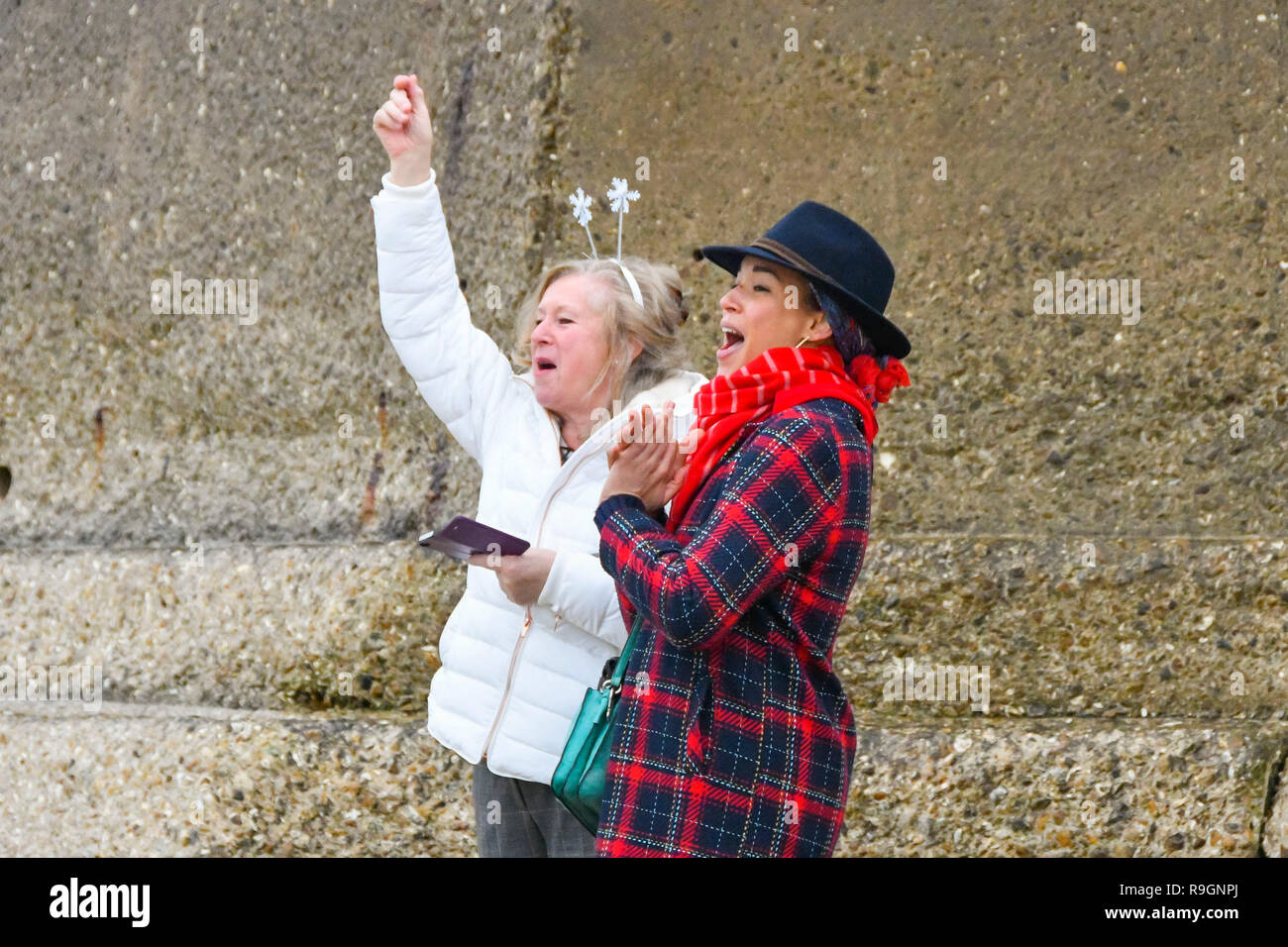 Charmouth, Dorset, UK. 25th Dec, 2018. Two women cheer on the Christmas day swimmers wearing fancy dress braving the chilly water to take a dip in the sea at Charmouth in Dorset to raise money for the RNLI. Picture Credit: Graham Hunt/Alamy Live News Stock Photo