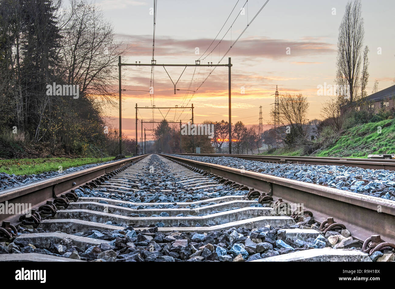 View between the two steel bars of a railroad track diminishing in the distance, in the Dutch province of Limburg, at sunset Stock Photo
