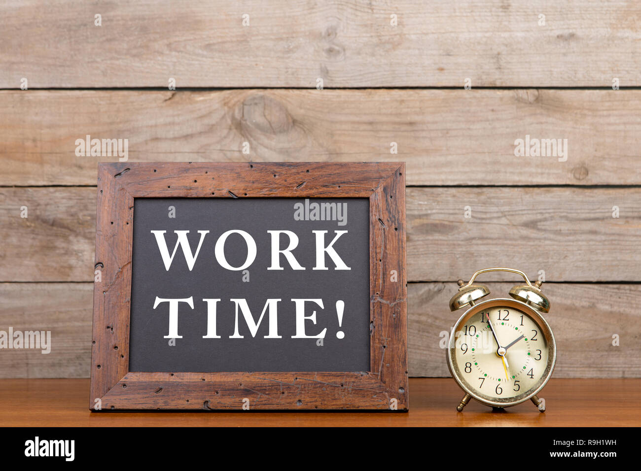 Alarm clock and blackboard with text 'Work time' on brown wooden background Stock Photo