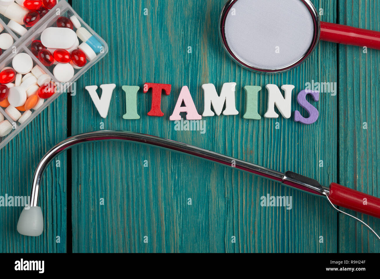 Text 'Vitamins' of colored wooden letters, stethoscope and pills on a blue wooden background Stock Photo