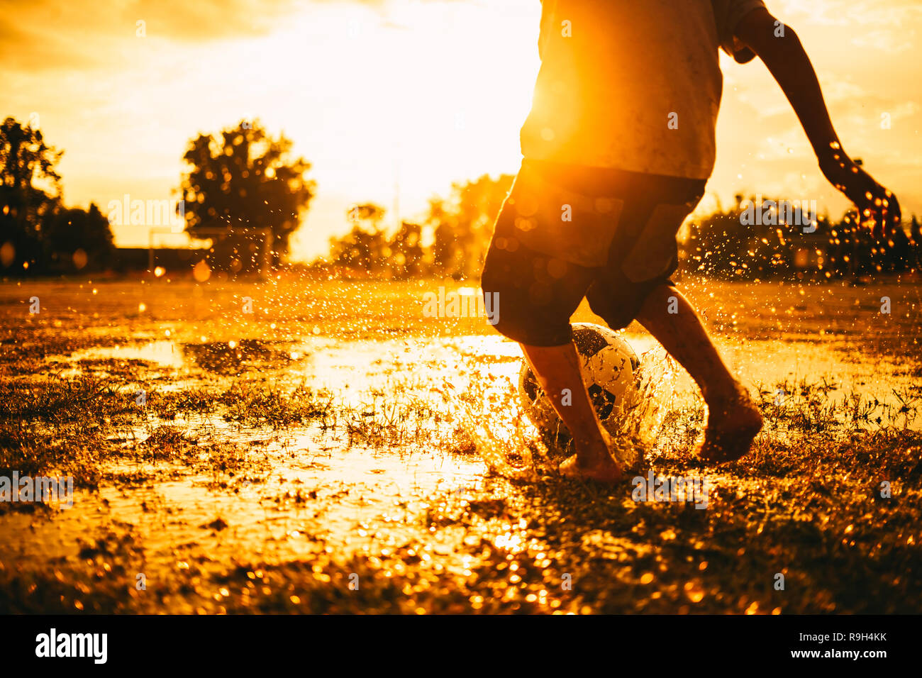 Action sport picture of kids playing soccer football among the rain for exercise in community rural area under the sunset. Stock Photo