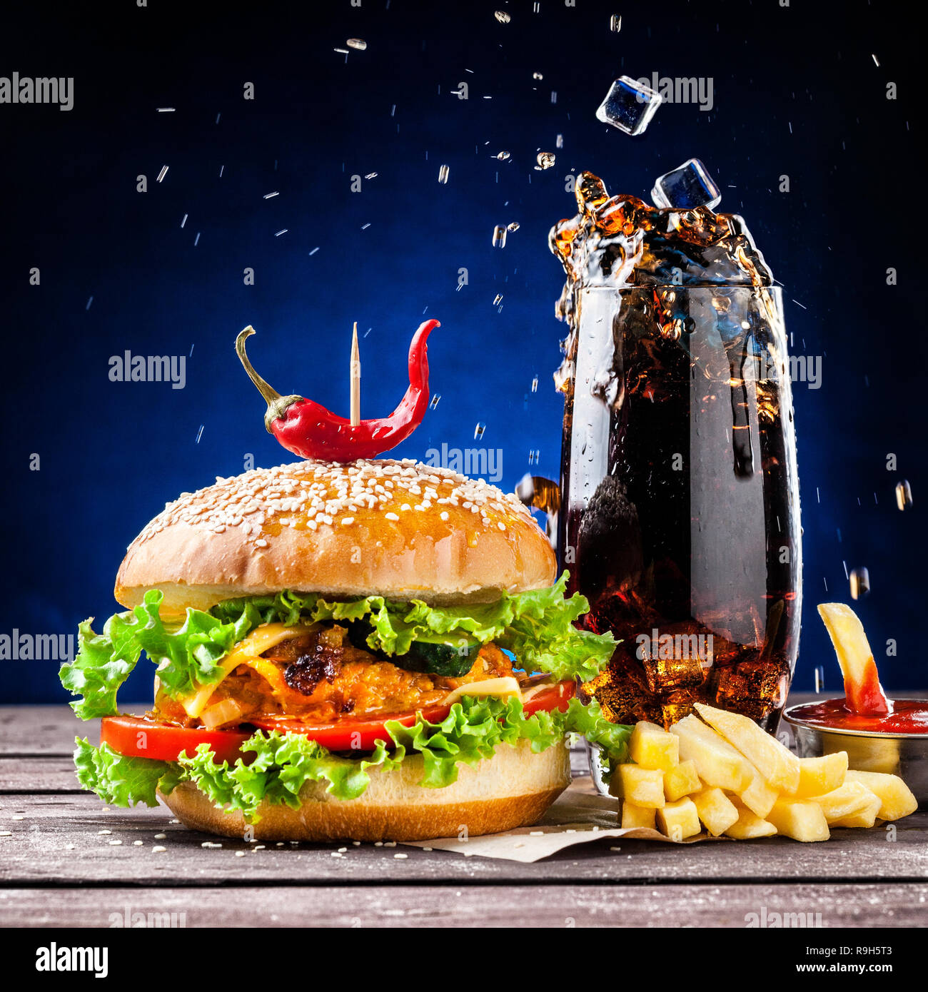 Veggie burger, French fries, ketchup and ice cubes falling in cola glass Stock Photo
