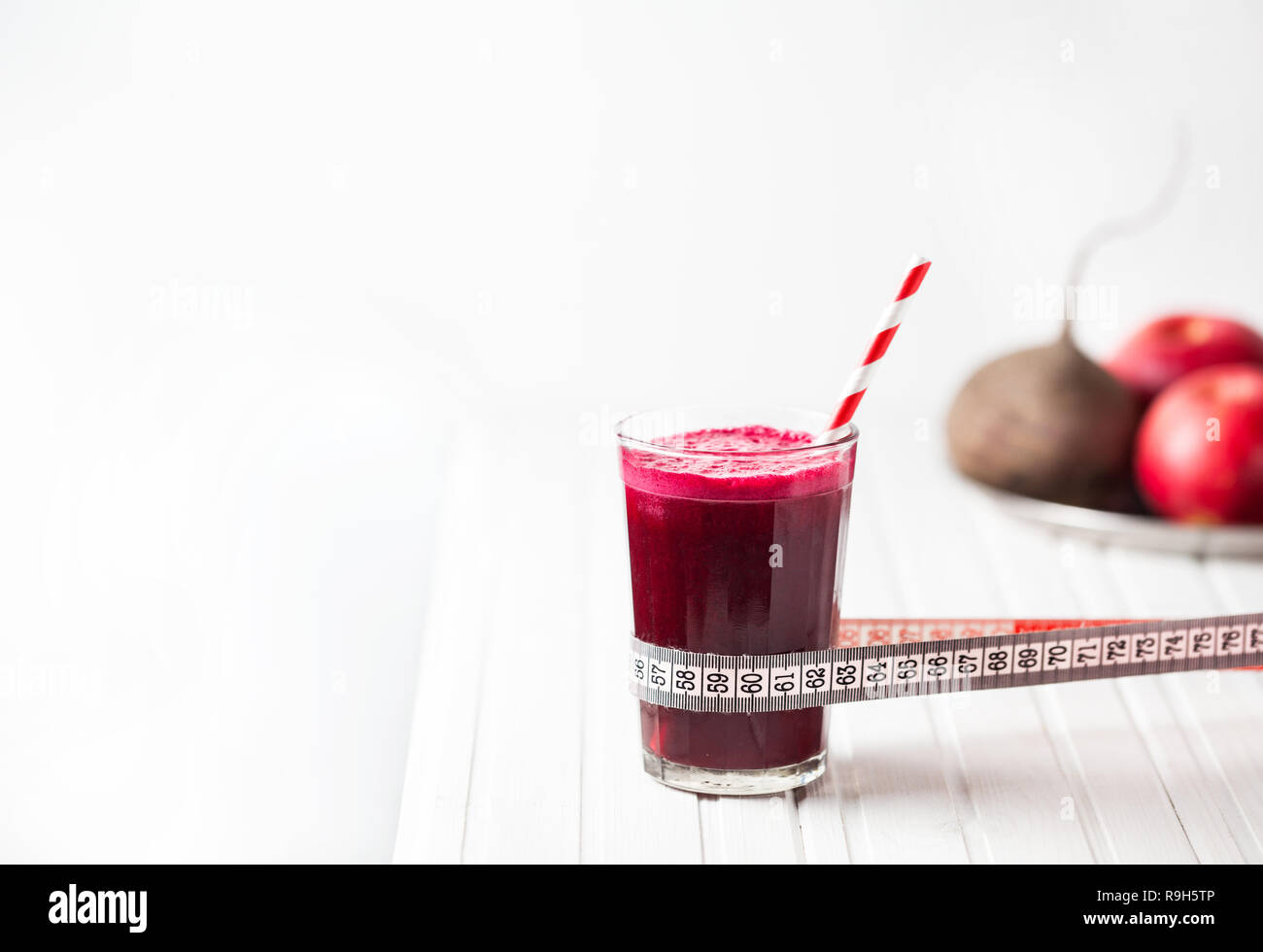 Fresh beetroot and apple juice in the glass with tape measure on white wooden background with space for text Stock Photo