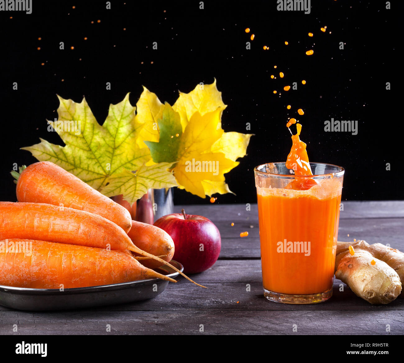 Fresh carrot, apple, ginger juice with splashes on wooden background in autumn season Stock Photo