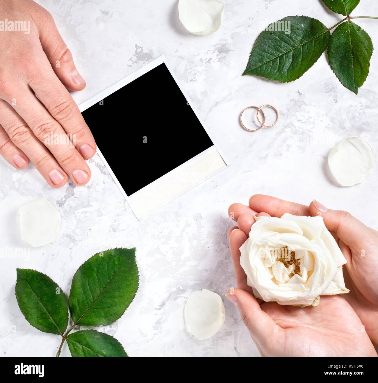 Blank photo frame, two wedding rings, bride and groom hands on white marble background Stock Photo